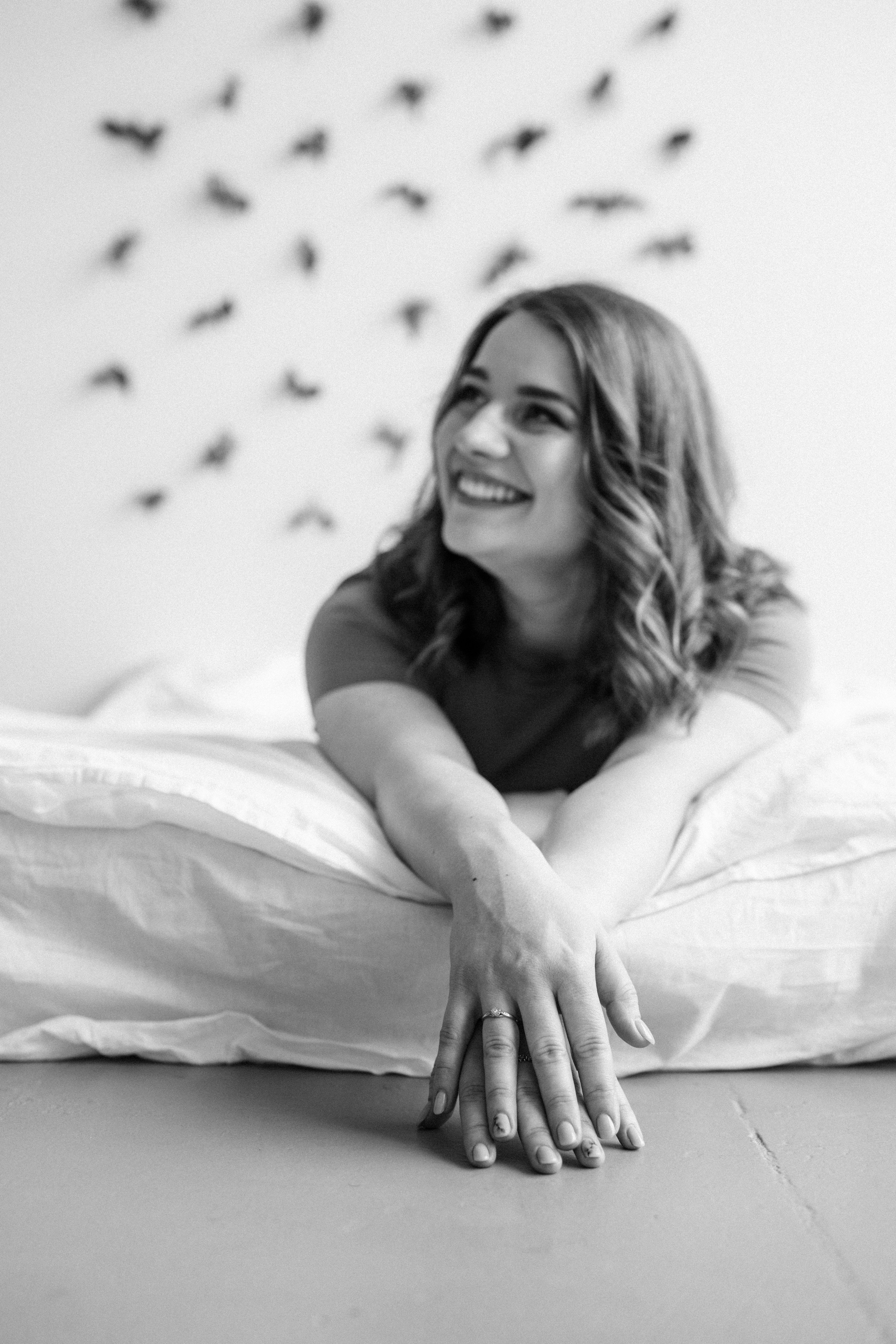 Художественный портрет молодой девушки; она лежит на кровати, вытянула руки вперед.