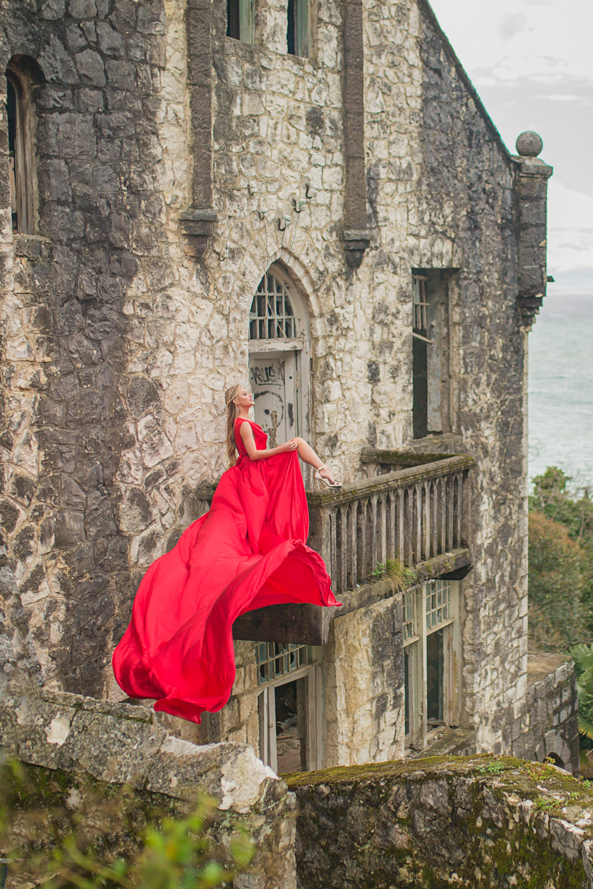 Девушка сидит в красном платье на балконе заброшенного здания