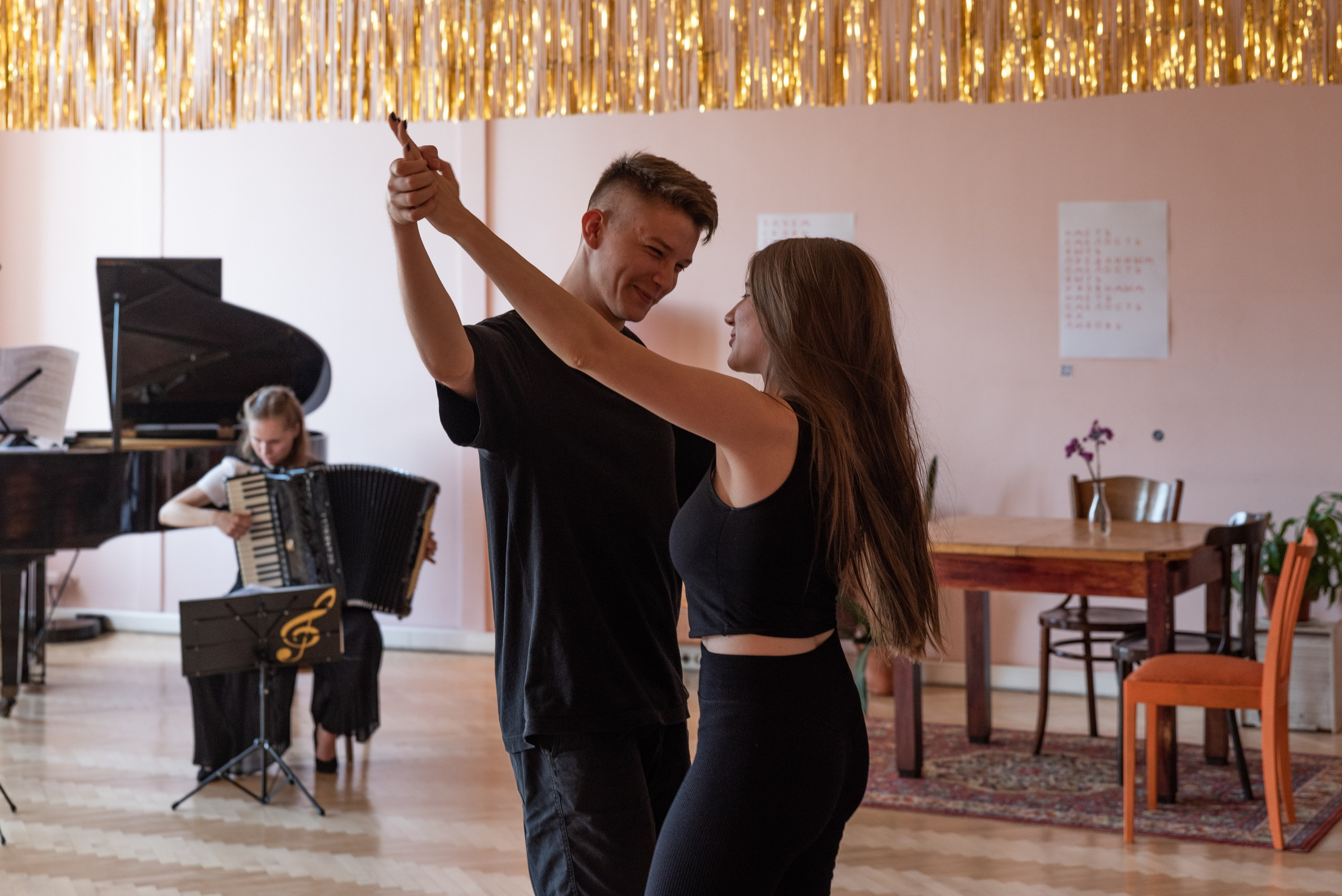 Молодой человек и девушка танцуют, на фоне девушка играет на аккордеоне.