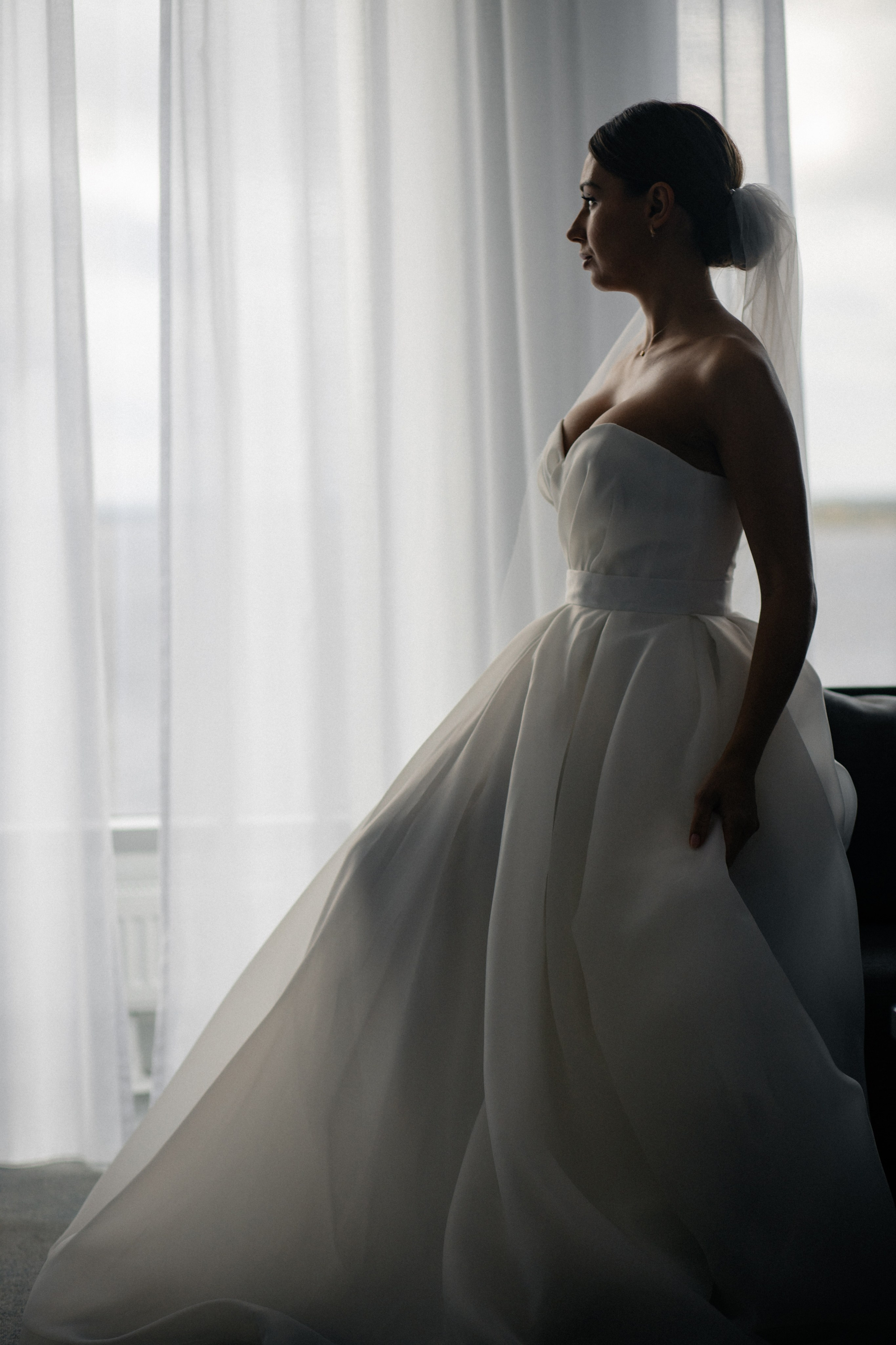 невеста сидит напротив  окна нежный естественный свет красиво подчеркивает ее силуэт 