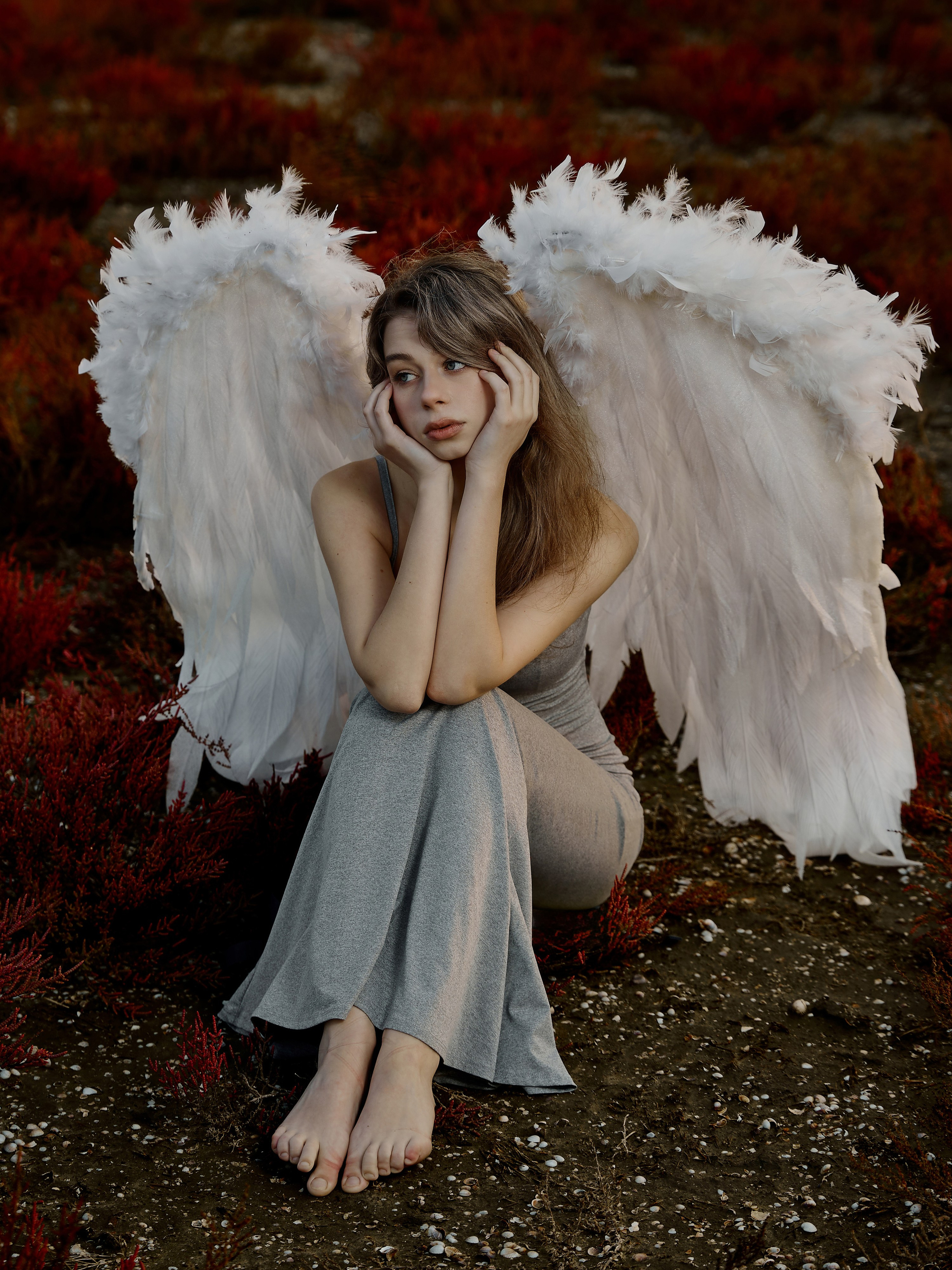 девушка с крыльями, ангел сидит на фоне красной растительности