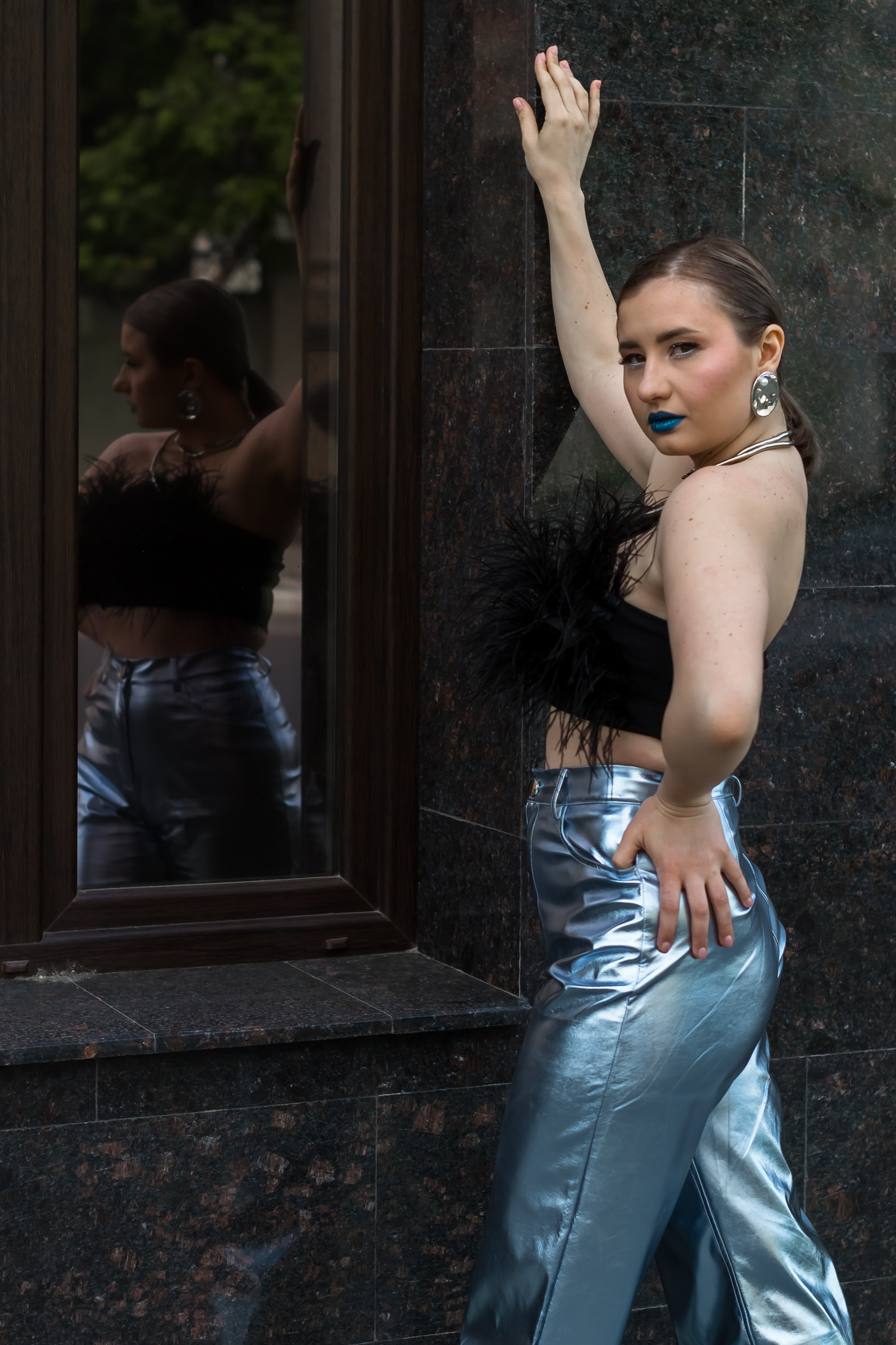 Портрет девушки в брюках стоит около стены.