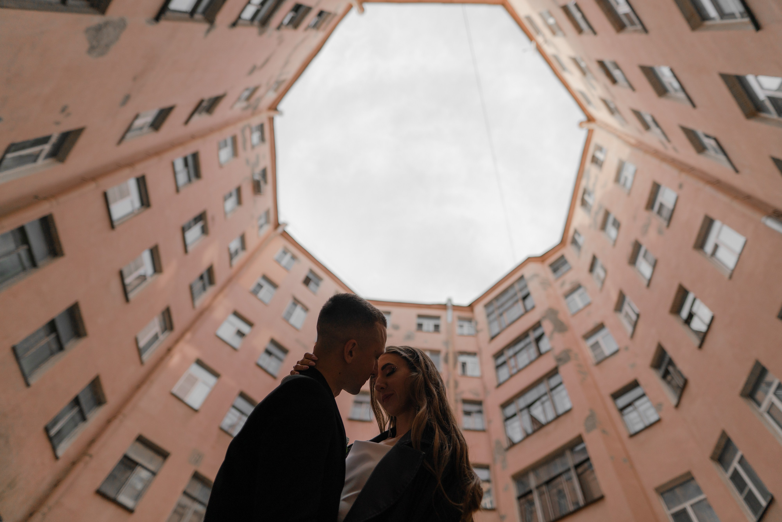 Жених и невеста стоят на фоне неба двора-колодца в центре Петербурге