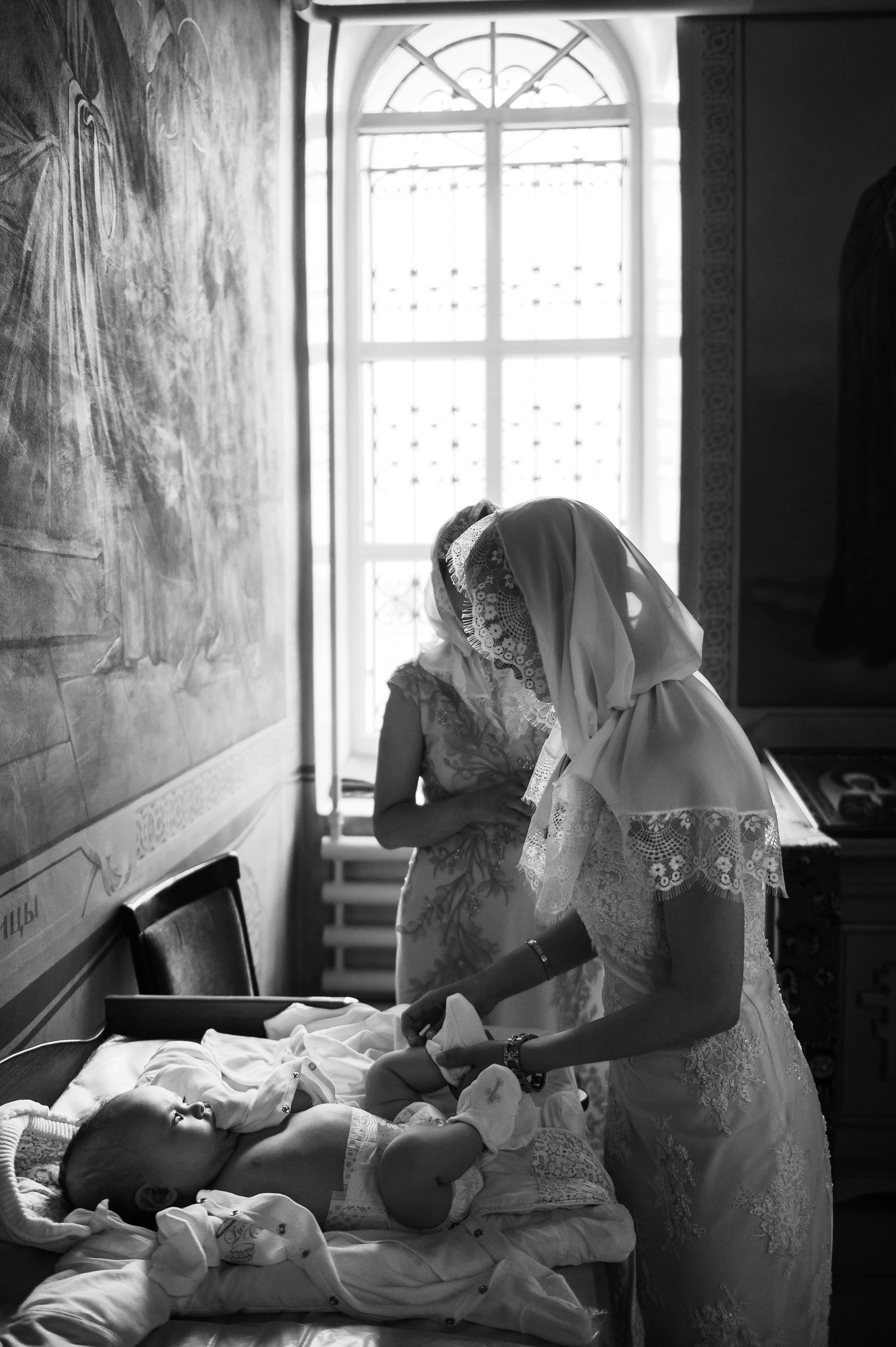 на фоне окна две женщины пеленают ребенка после крещения