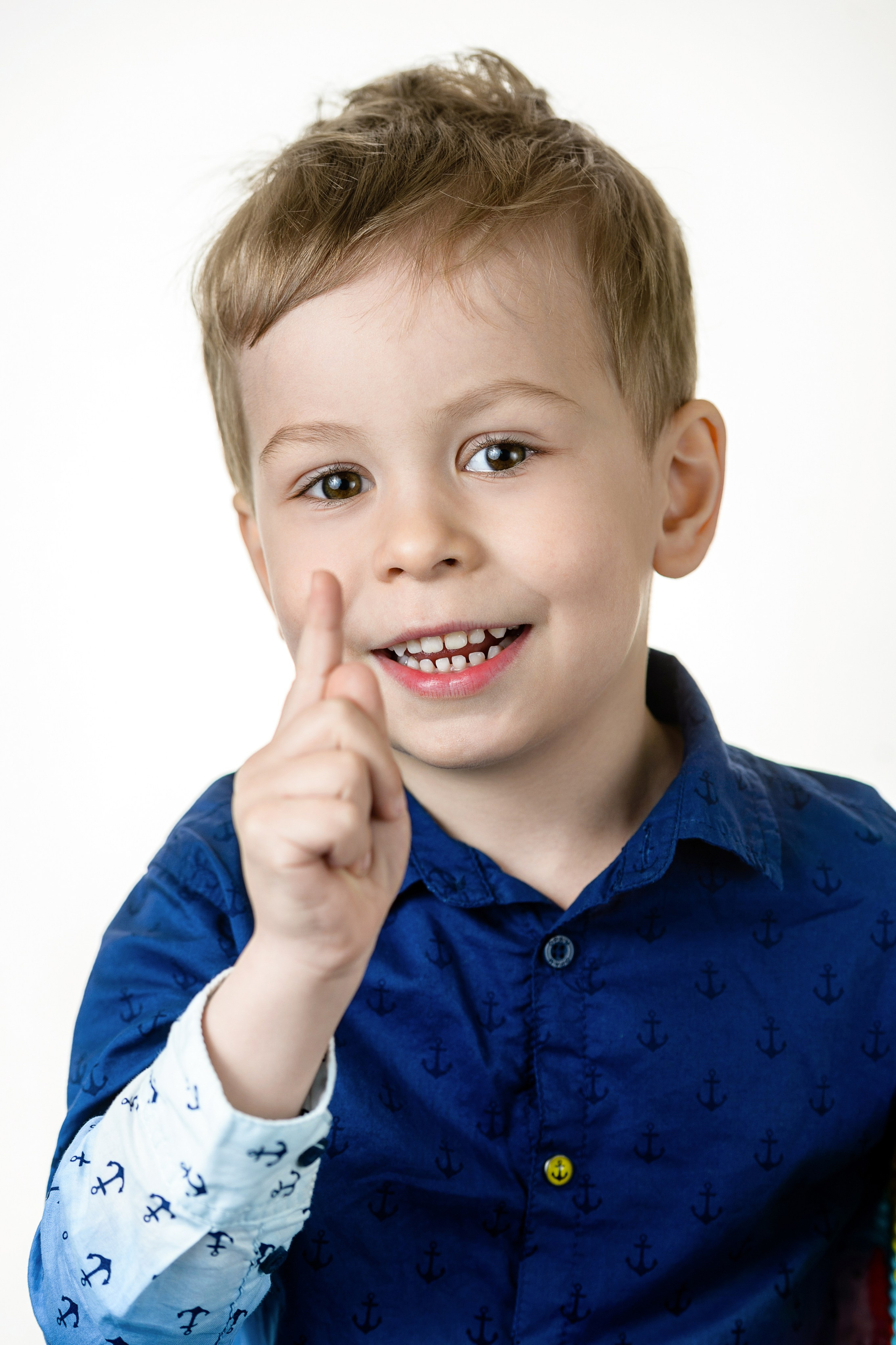 Портрет мальчика в синей рубашке на белом фоне, улыбается и держит руку у лица