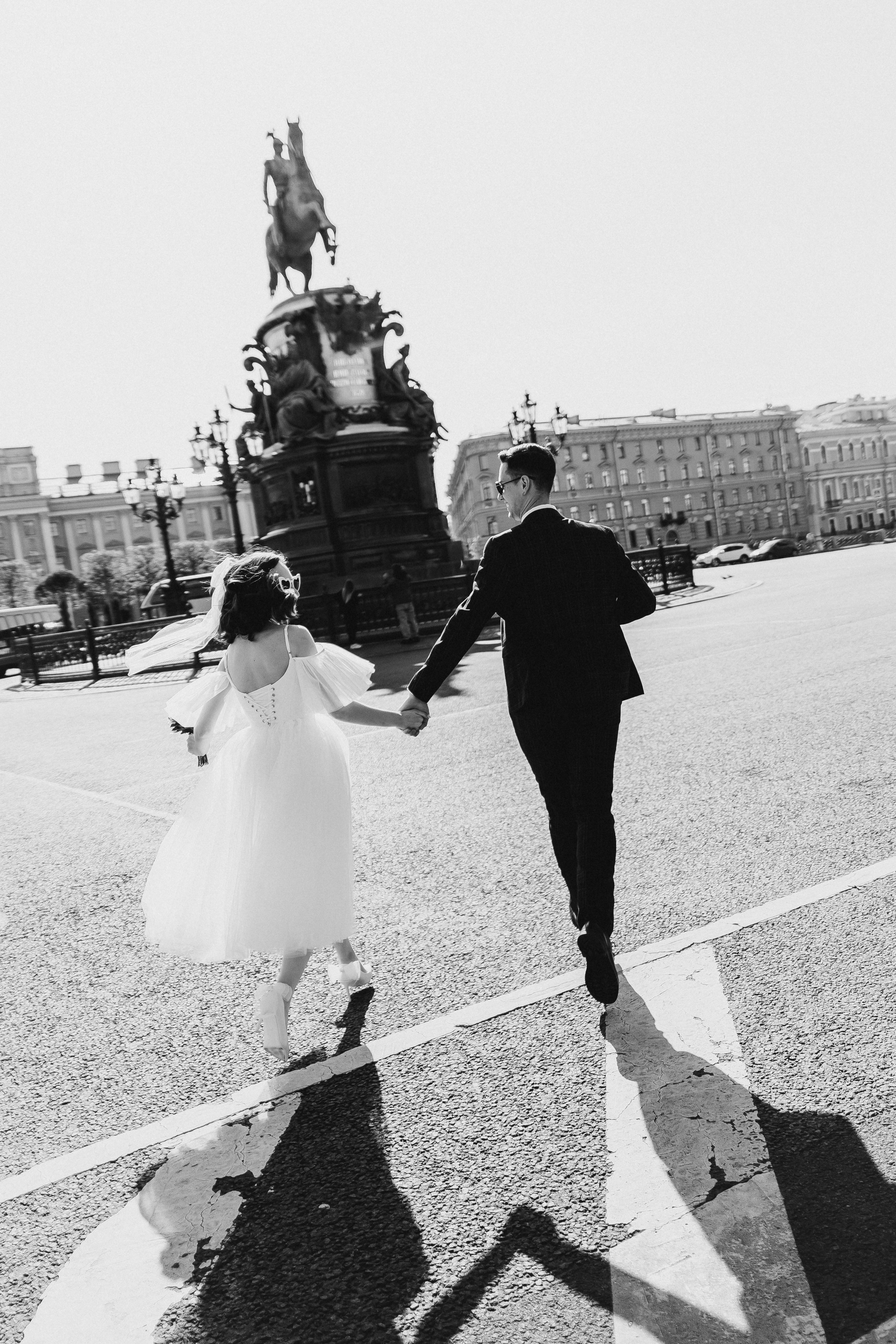 Черно-белая фотография бегущего жениха и невесты в центре города