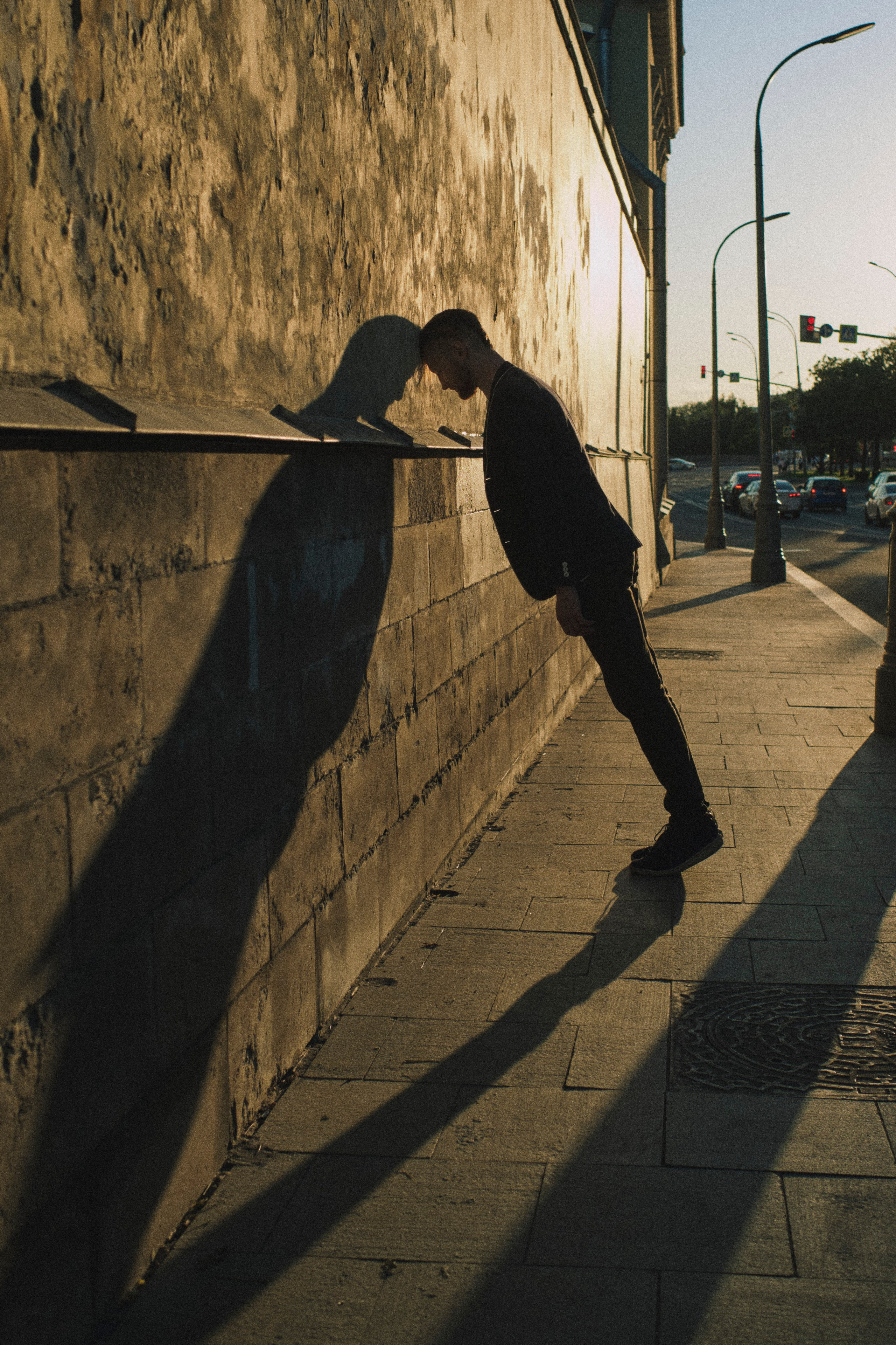 Мужчина облокачивается на стену на закате, давая длинную тень