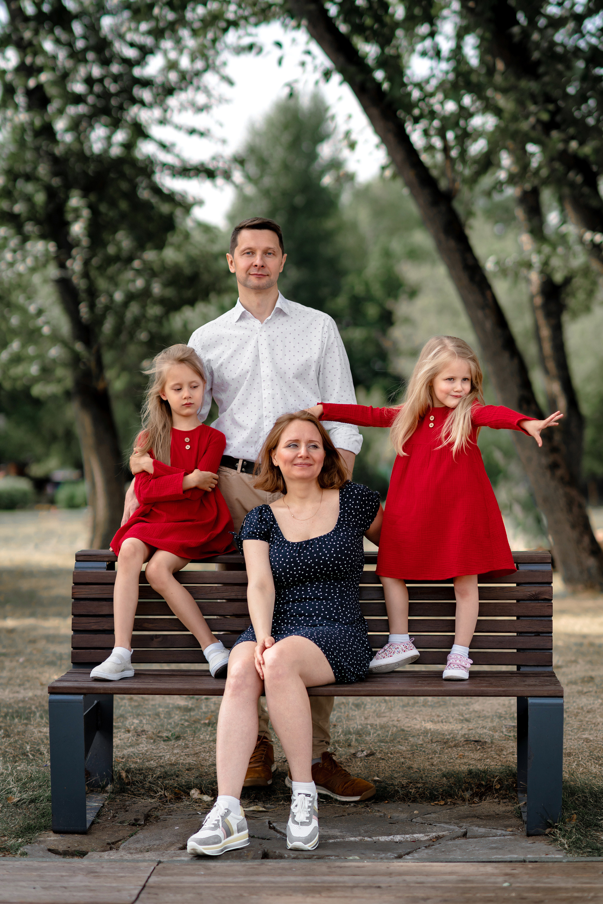 Красивая семья на скамейке в парке, две дочери в красных платьях