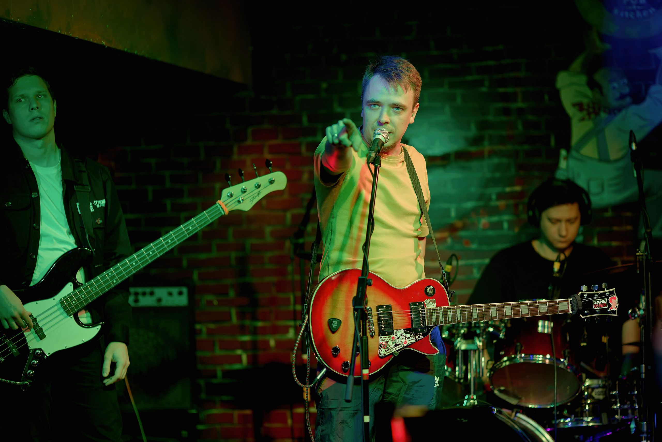 Рок-группа на сцене - вокалист с гитарой, бас-гитарист и барабанщик, живое выступление в клубе, концертный фотограф