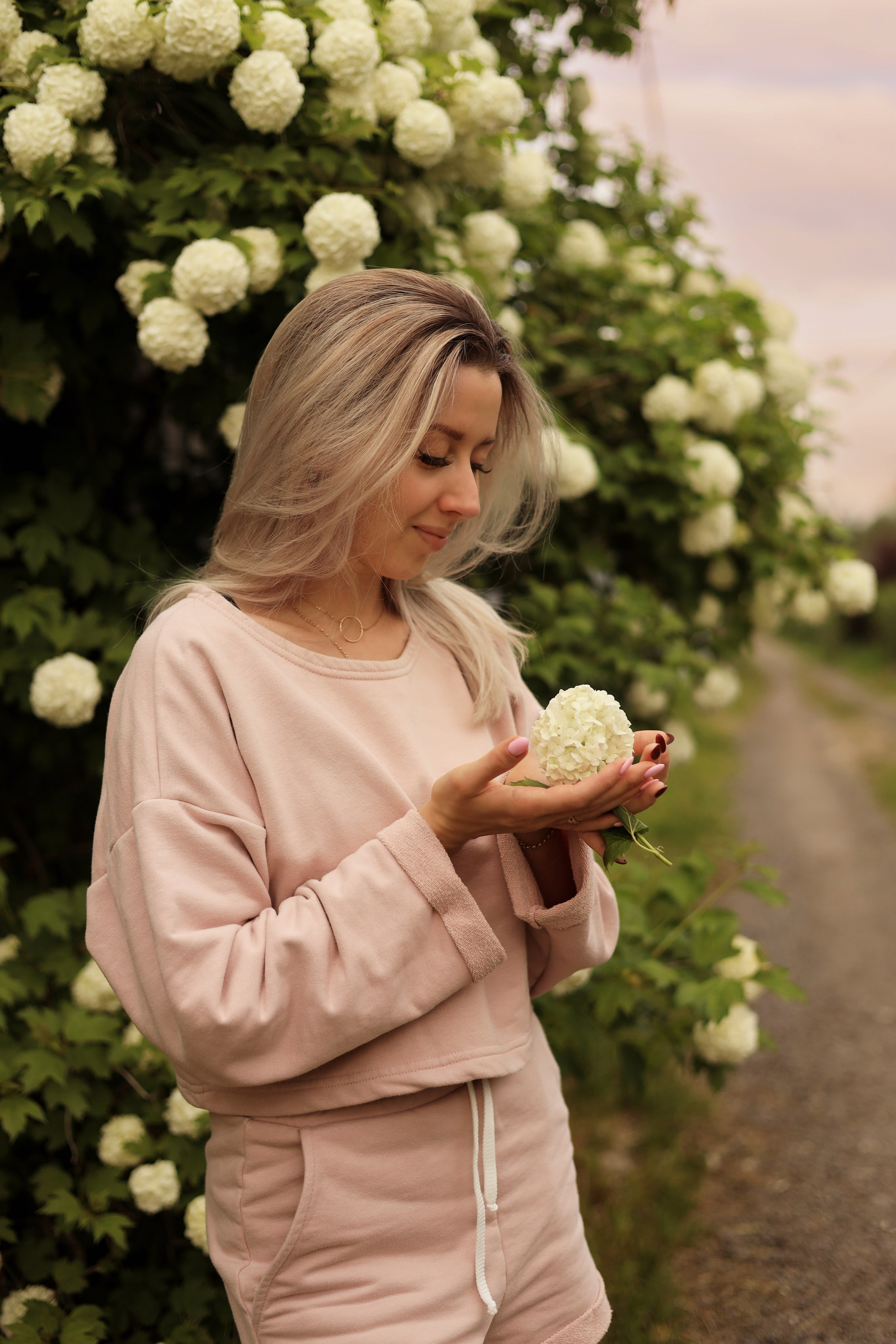 девушка на фоне цветов держит цветок в руках на фотосессии