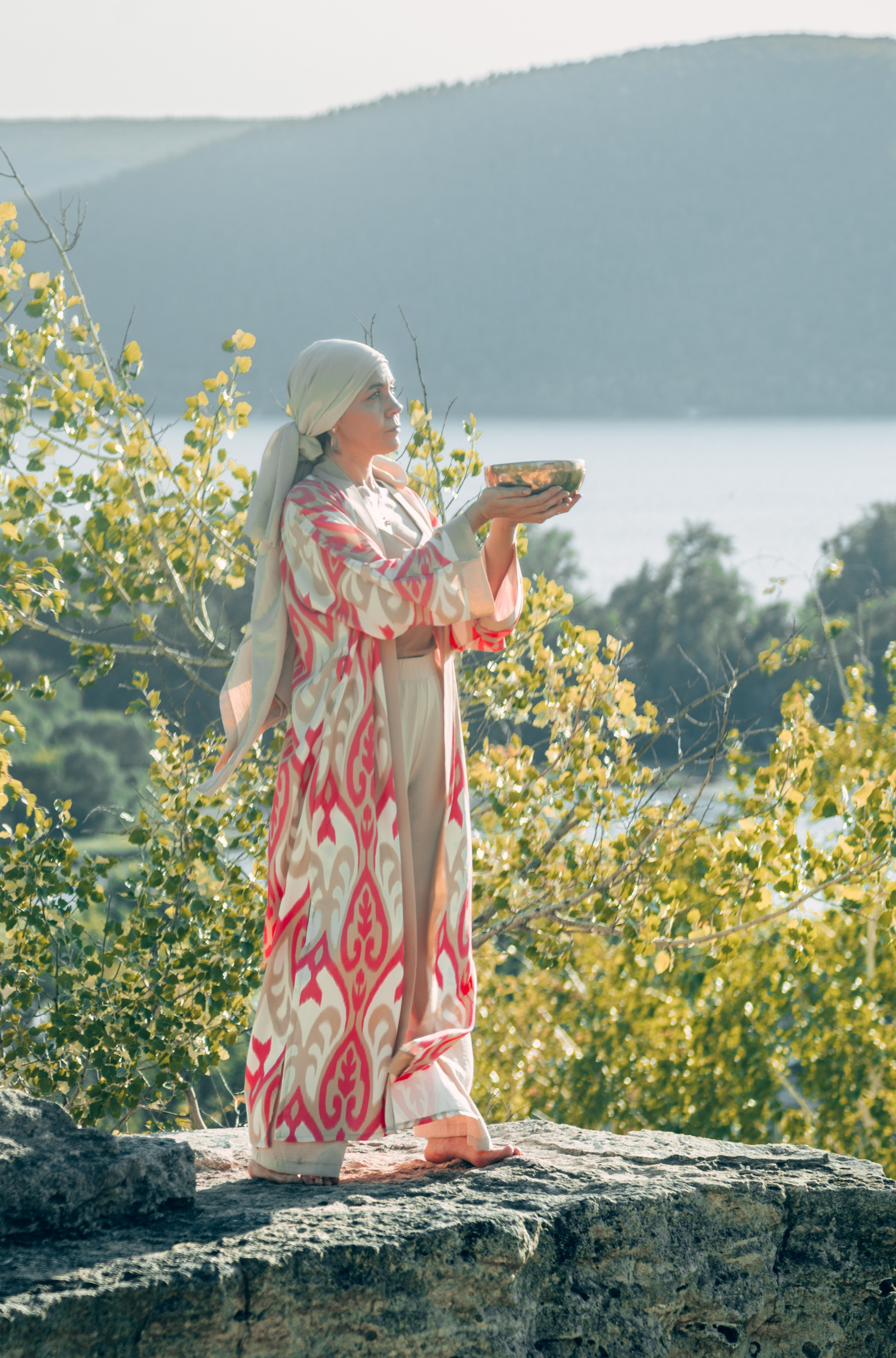 Женщина в этническом халате на фоне природы Самары с чашей в руках