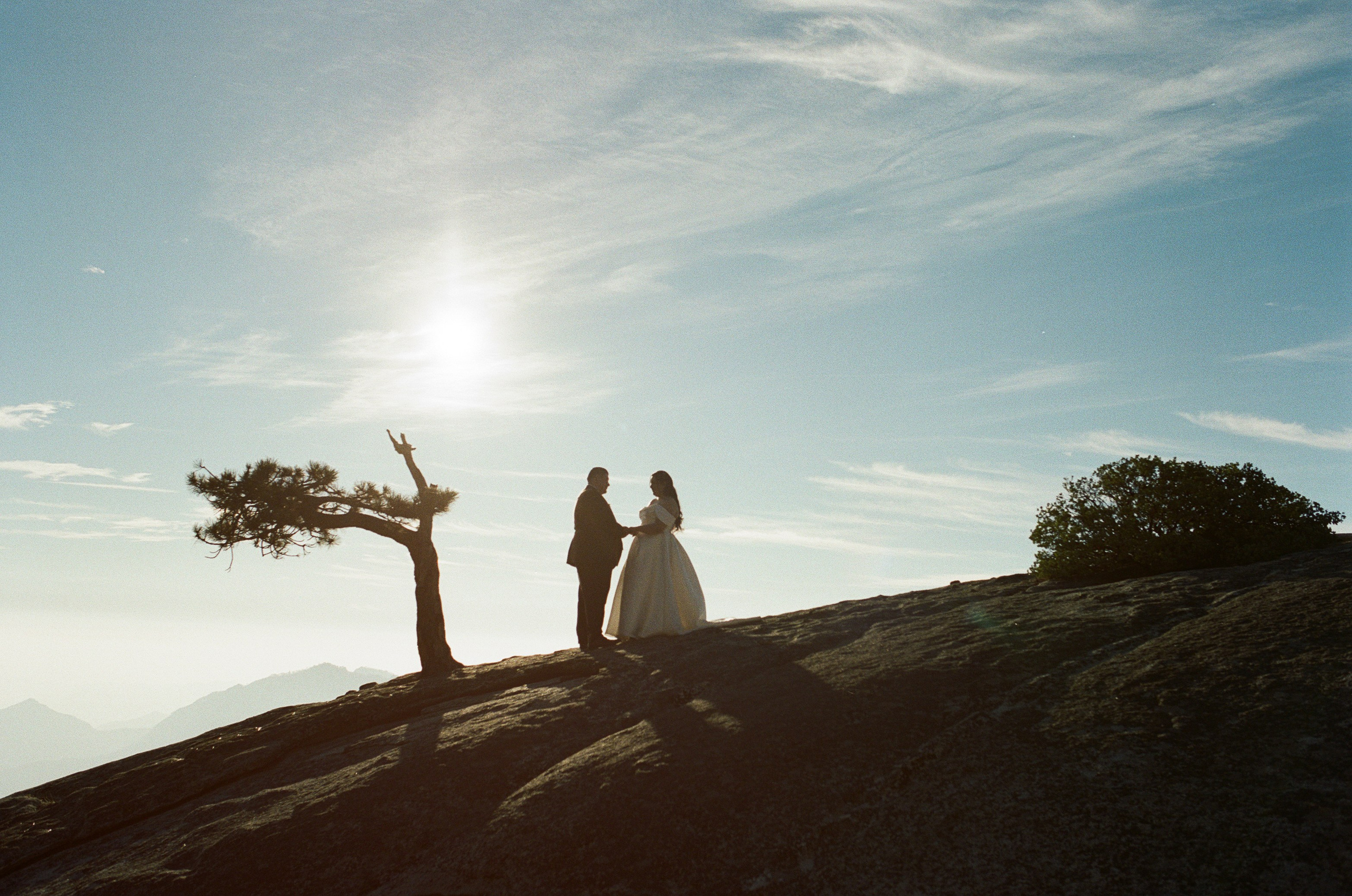 a landscape photo of a bride and groom walking on top of the mountain during sunset
