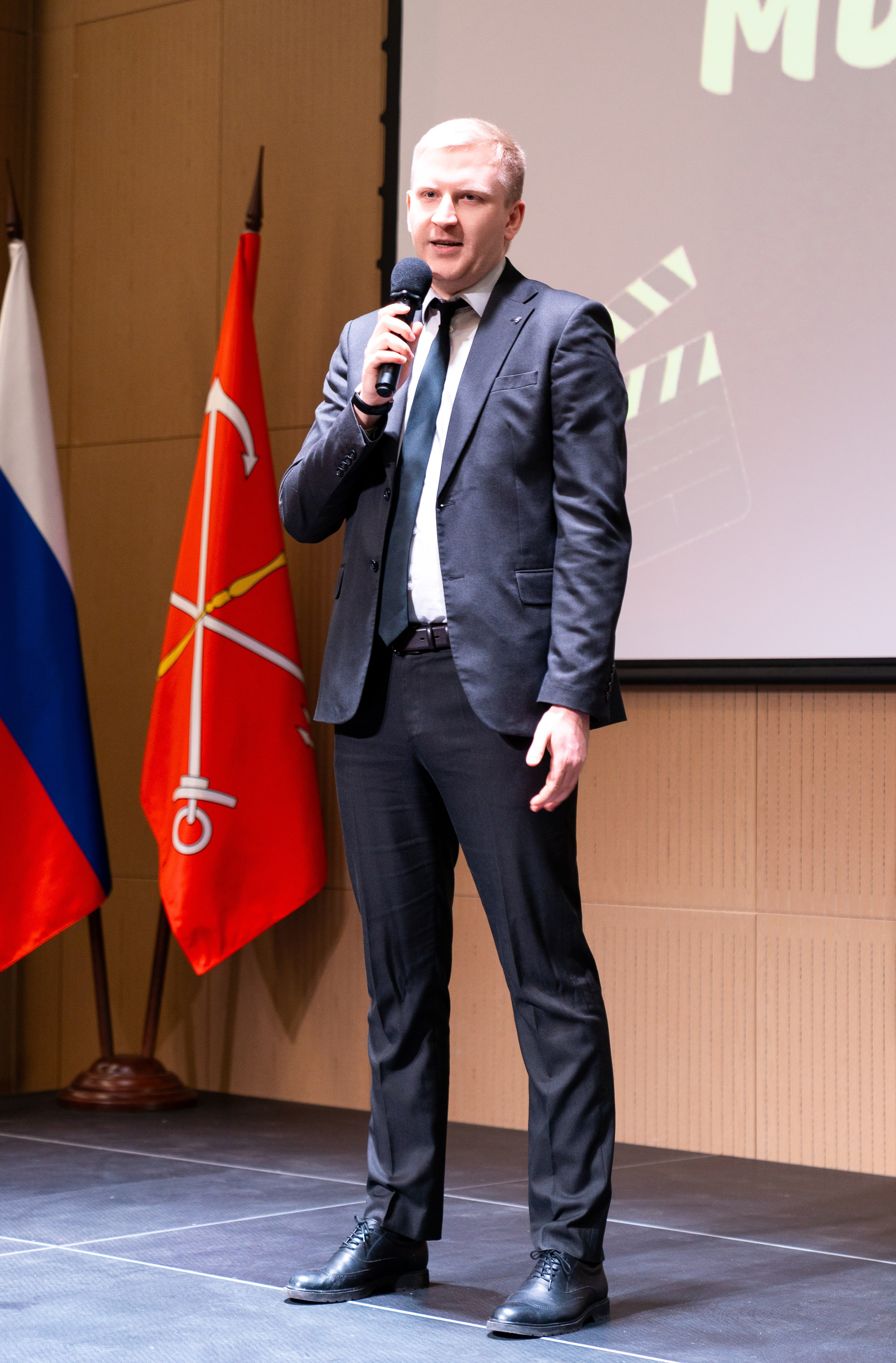 Глава района на  инклюзивном балу  «Мы все равны» выступает со сцены с микрофоном. На фоне флаг России. Фото Мальцев Евгений.