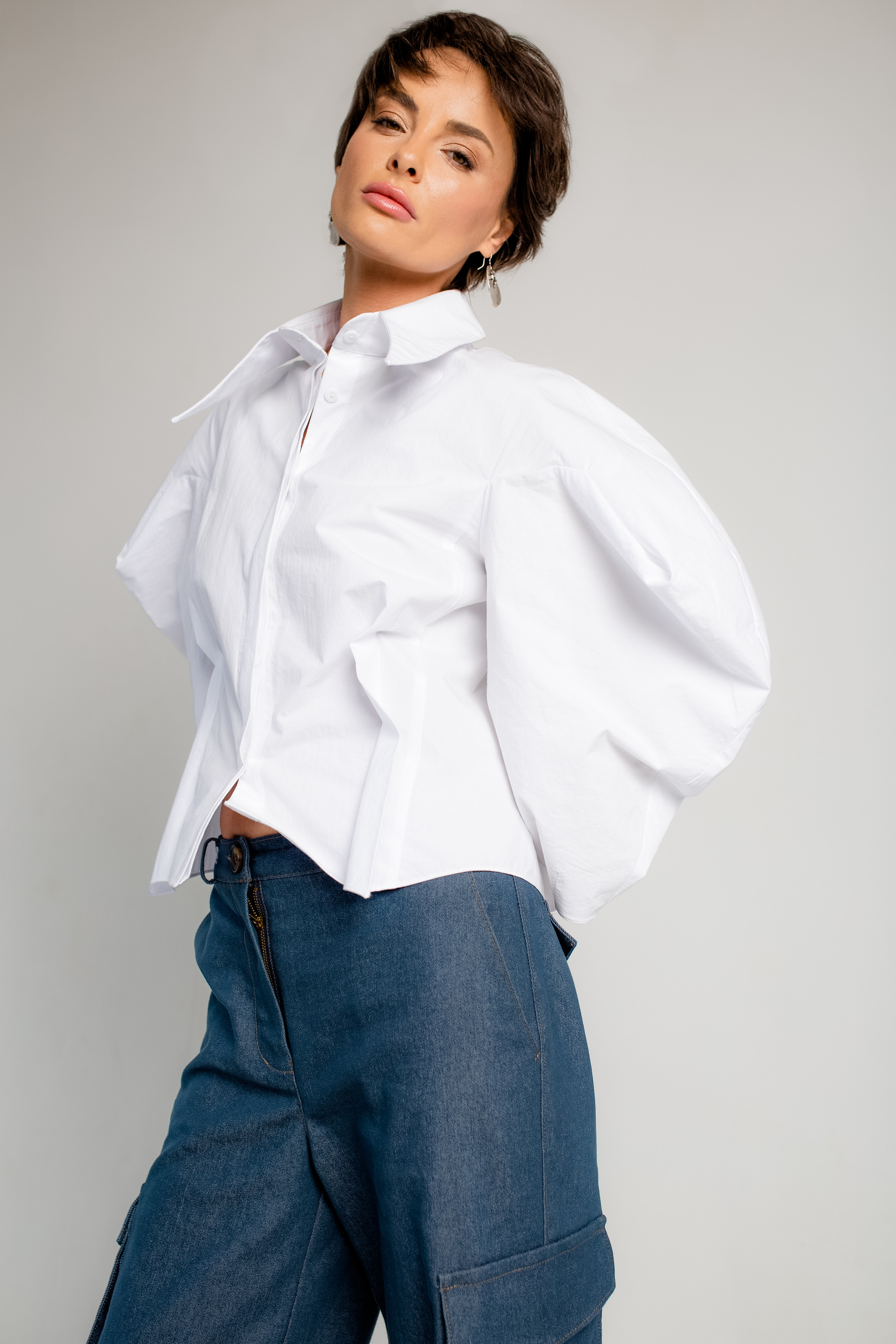 Фотомодель в белой рубашке и синих брюках позирует на фотосессии для бренда женской одежды.