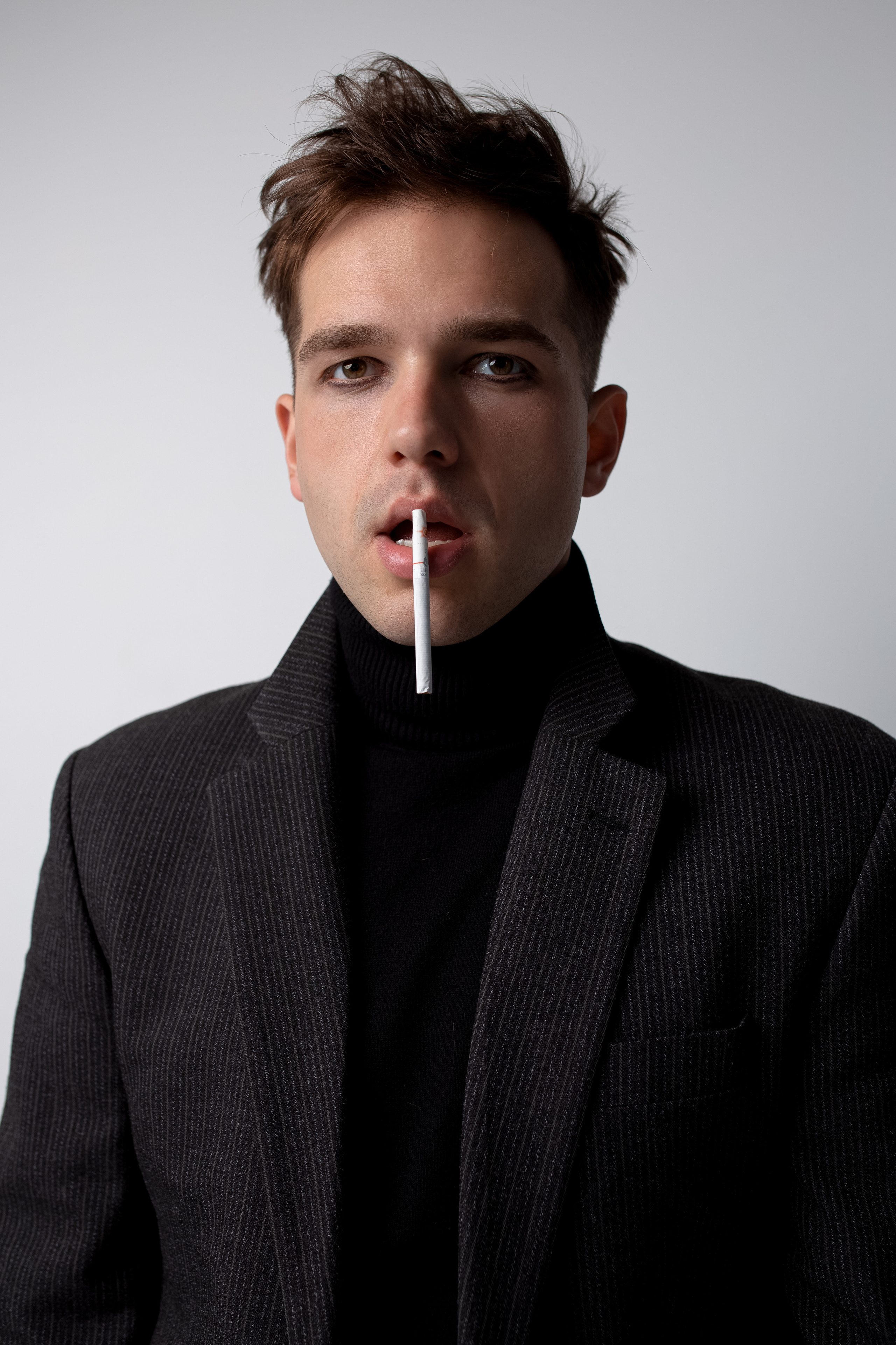 Парень в пиджаке и чёрной водолазке приклеил к нижней губе сигарету
