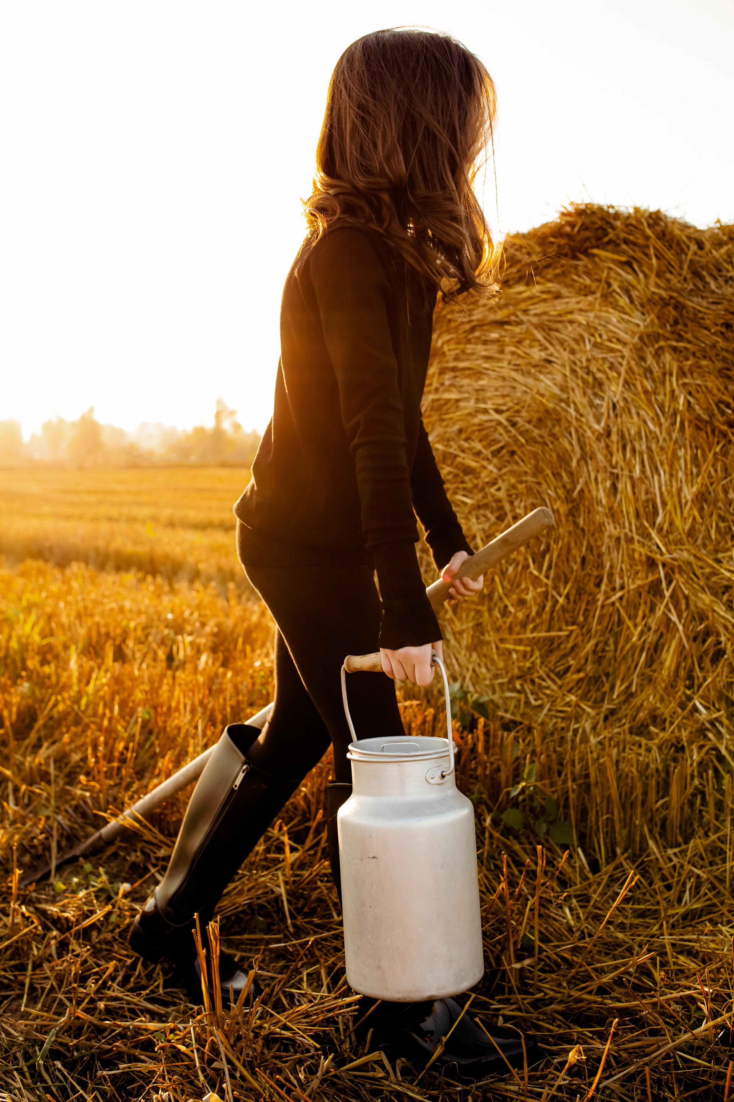 Фотосессия девочки на закате в поле со стогами сена  с бидоном и граблями.