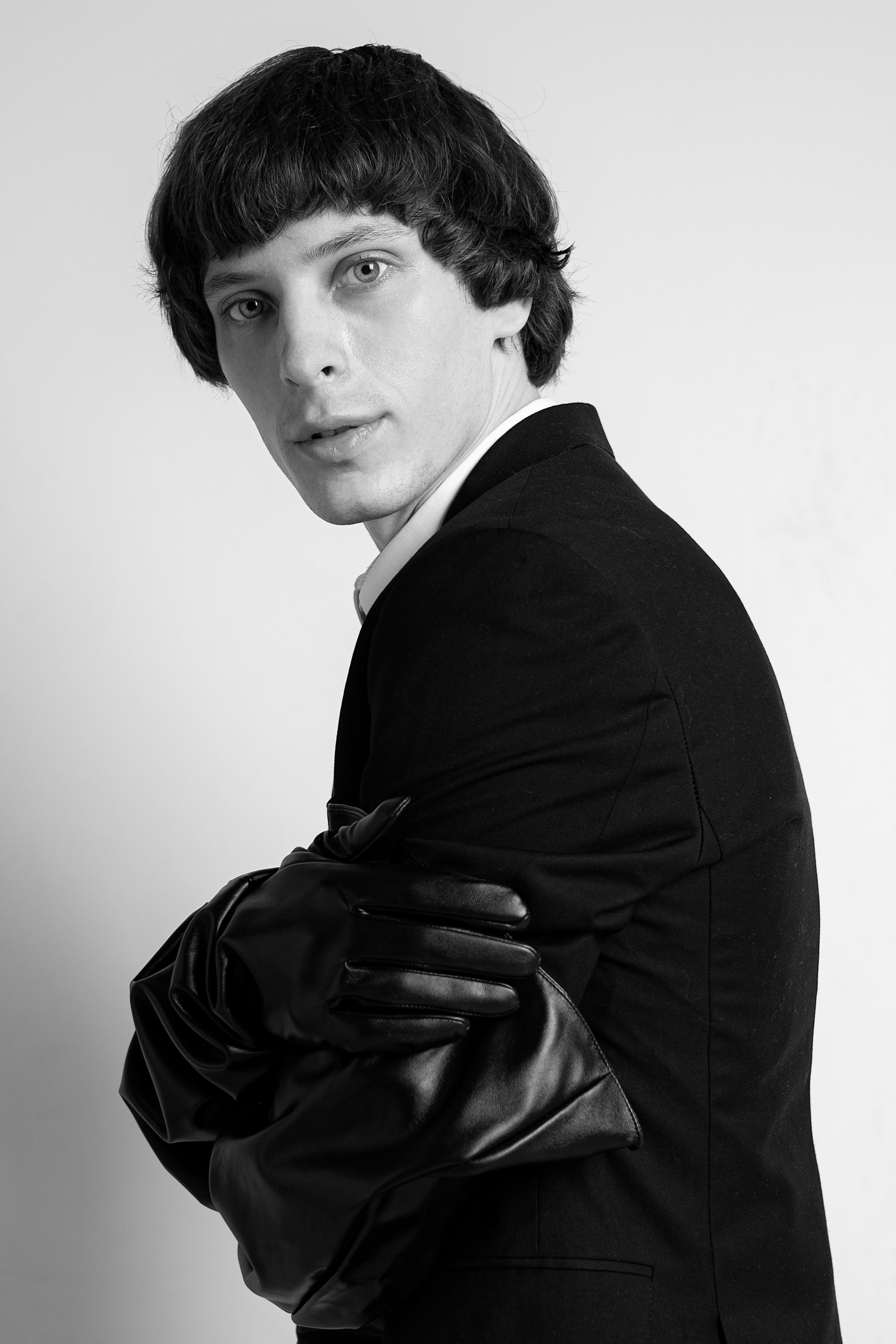 Стильный мужской чёрно-белый портрет. Парень в кожаных чёрных перчатках стоит боком к камере 