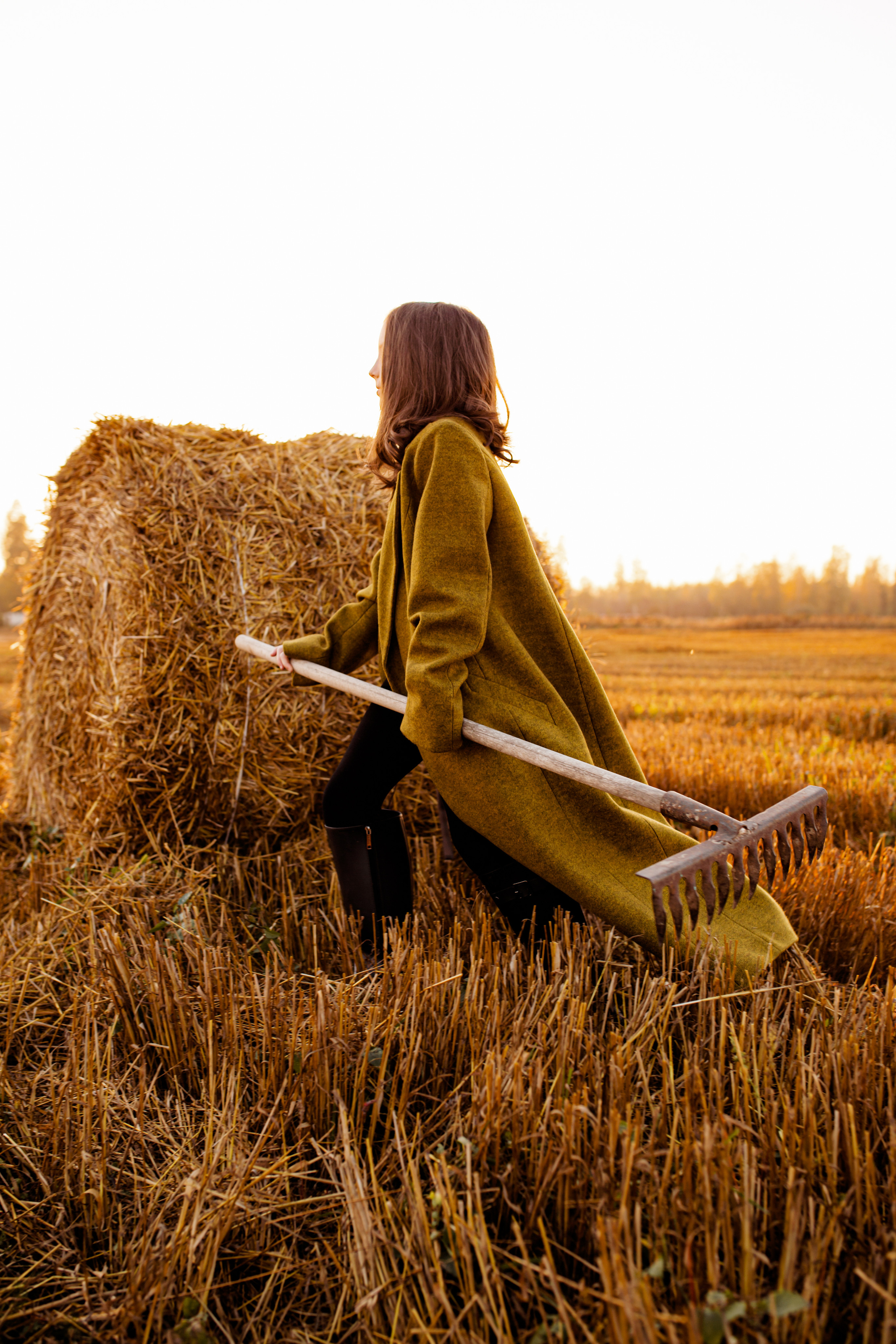 Девочка с граблями идёт по пол. в пальто мимо стогов сена.