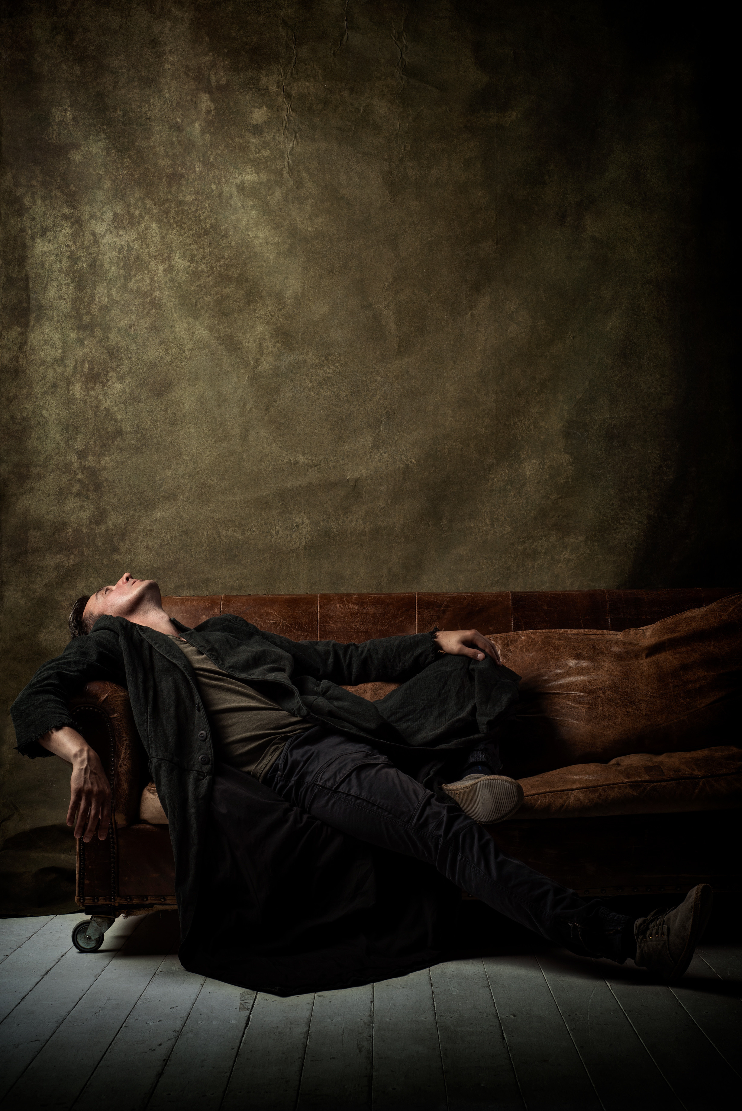 классический мужской портрет в коричневых тонах, мужчина в пальто лежит на кожаном диване 