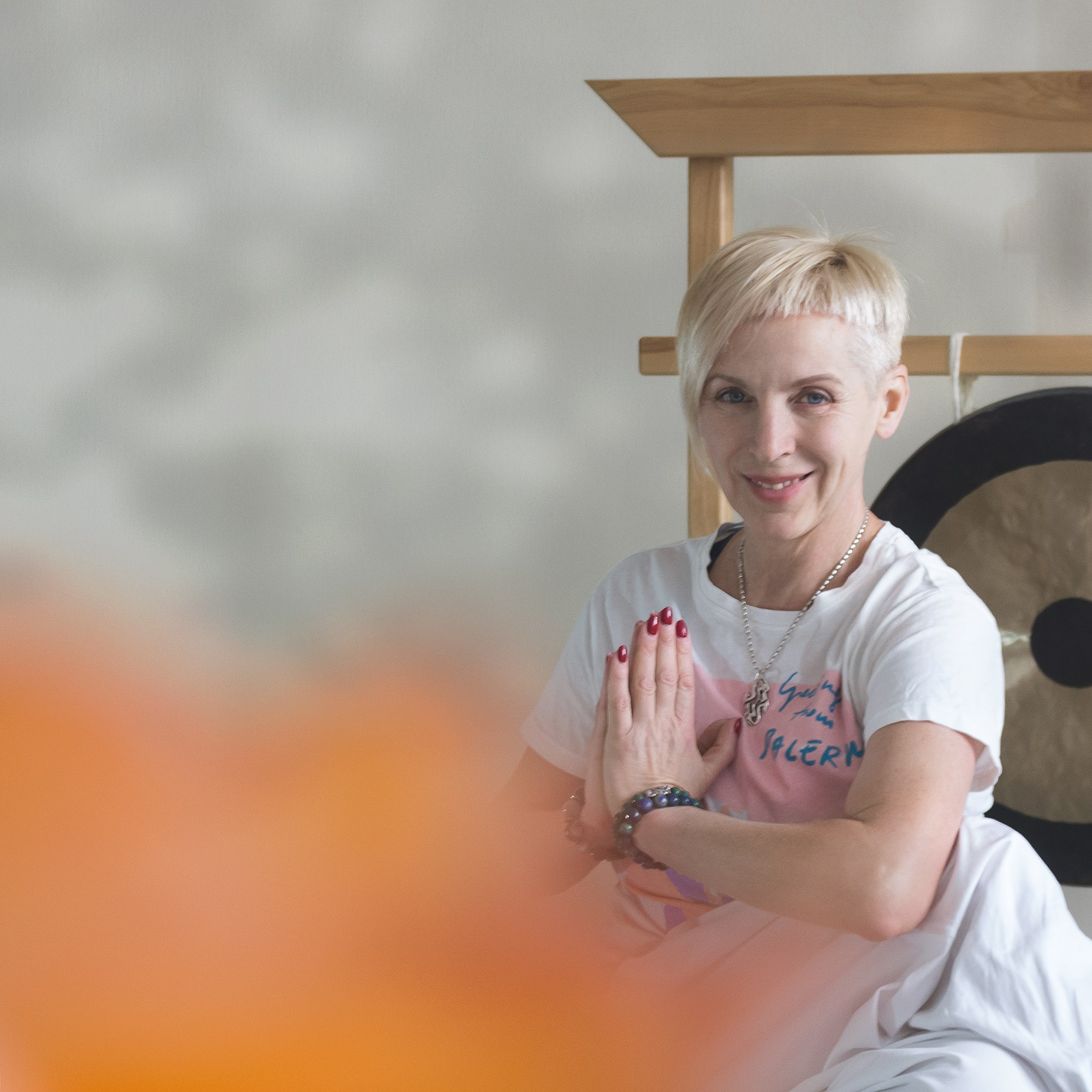 Портрет инструктора йоги. Женщина с короткой стрижкой, руки сложены в намасте. На заднем плане гонг.