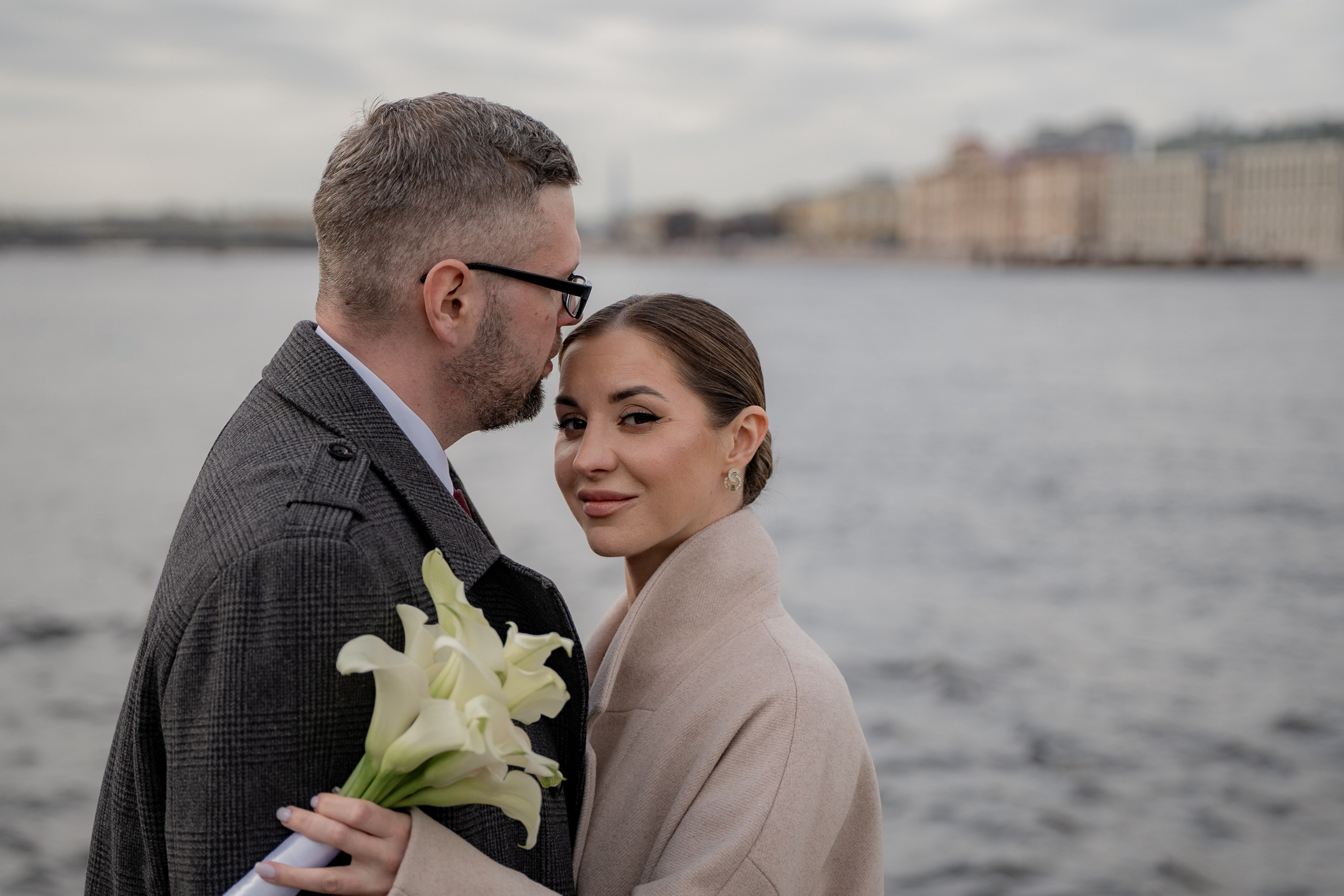 Свадебная фотосессия на набережной Невы недалеко от Дворца бракосочетания №2 невеста смотрит в камеру и обнимает жениха.