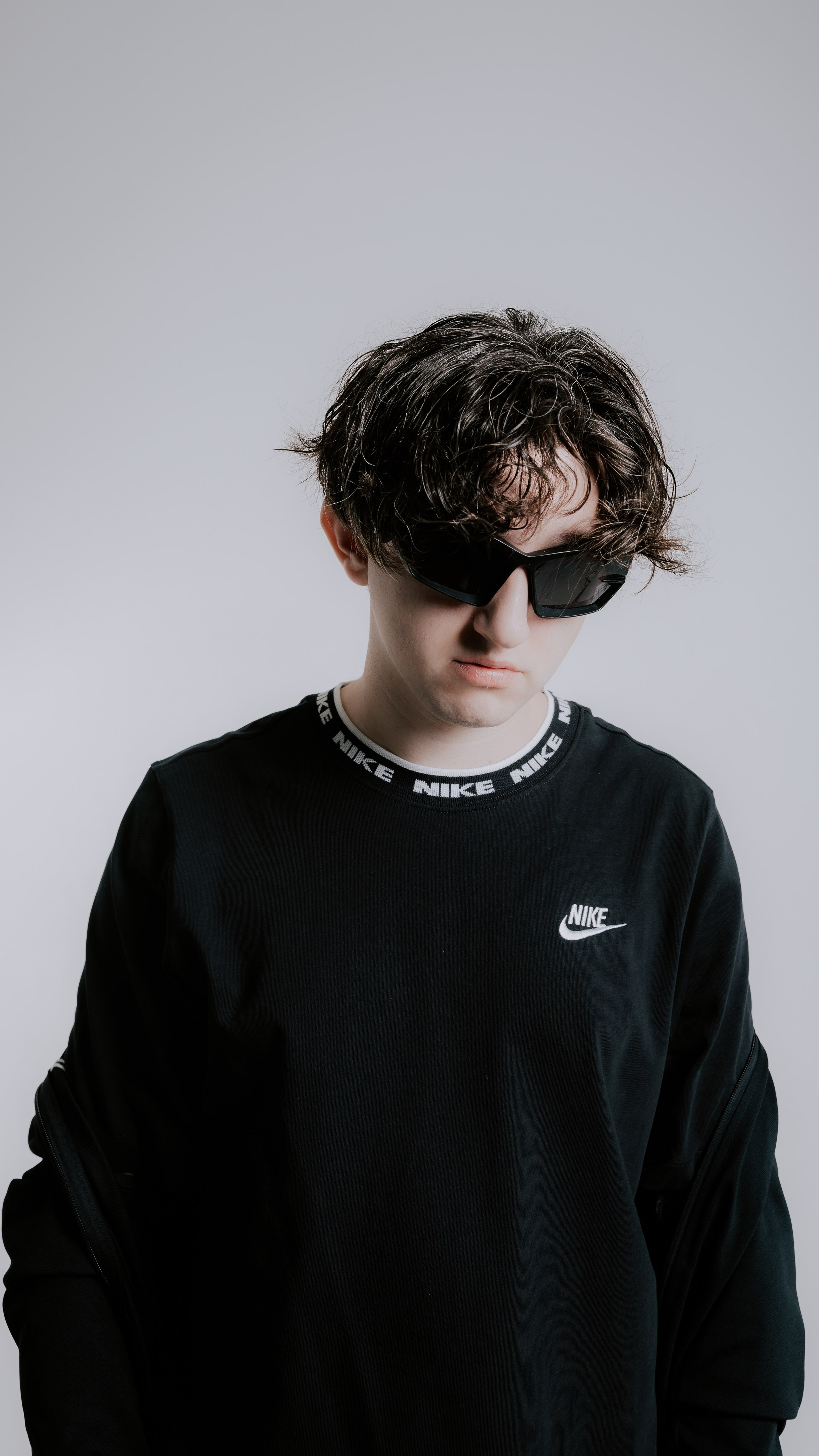 парень на белом фоне в очках и стильной прической в одежде от nike