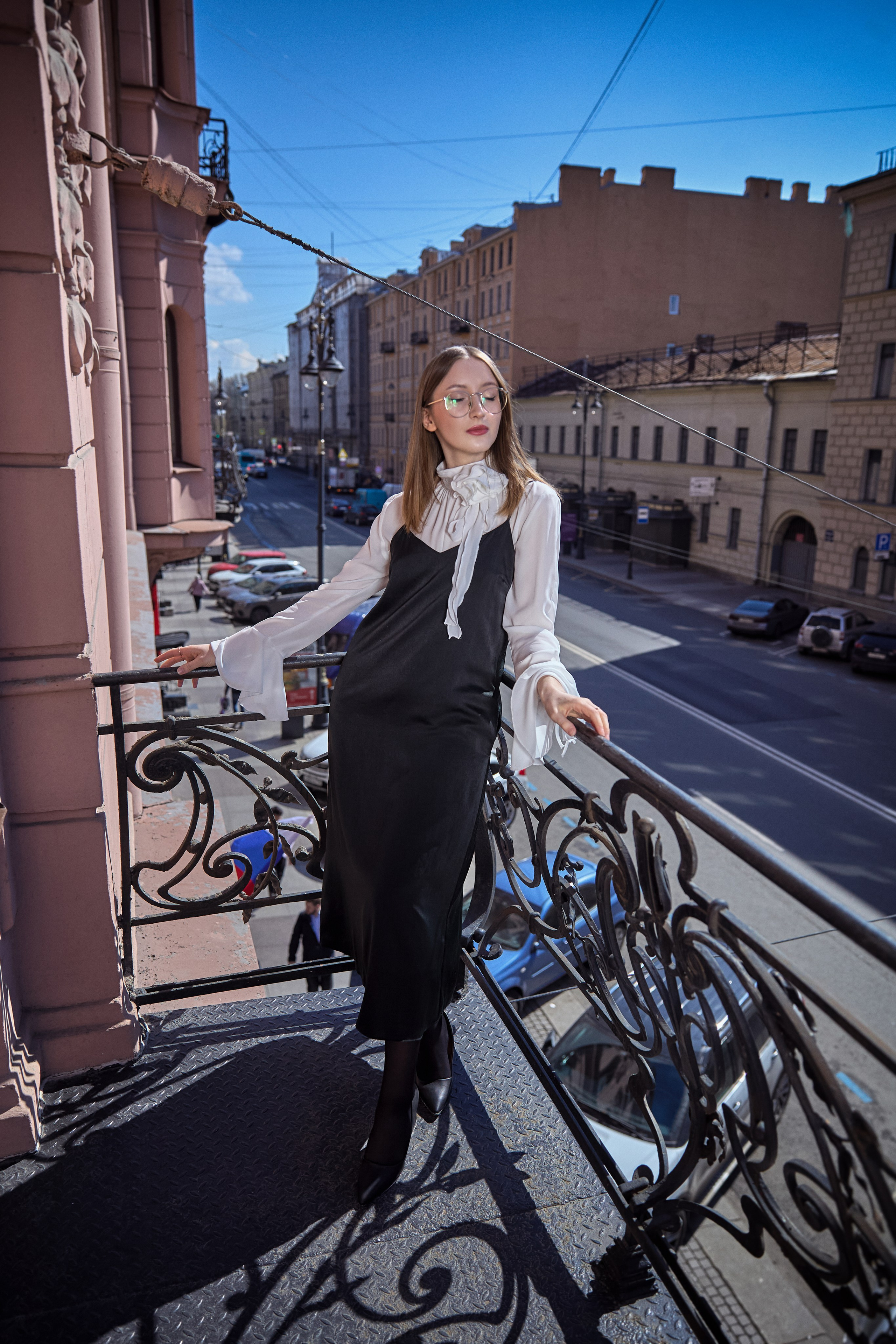 Девушка в блузе и сарафане на балконе на фоне улиц Петербурга