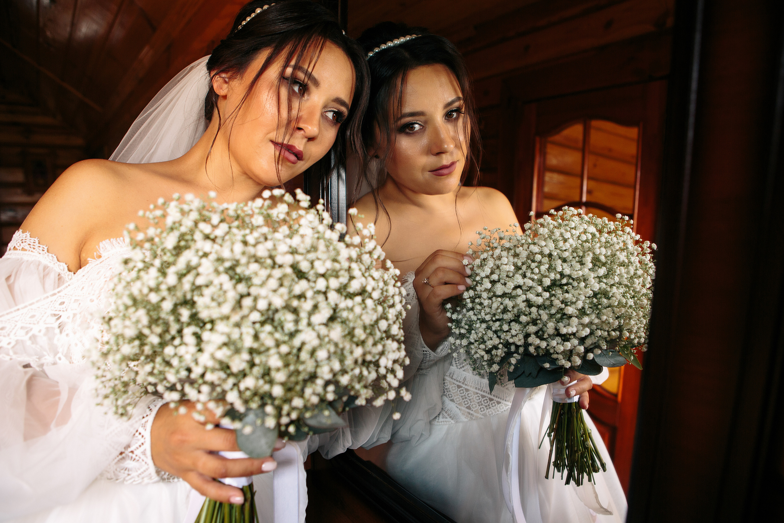 Невеста с букетом у зеркала в красивом свадебном платье