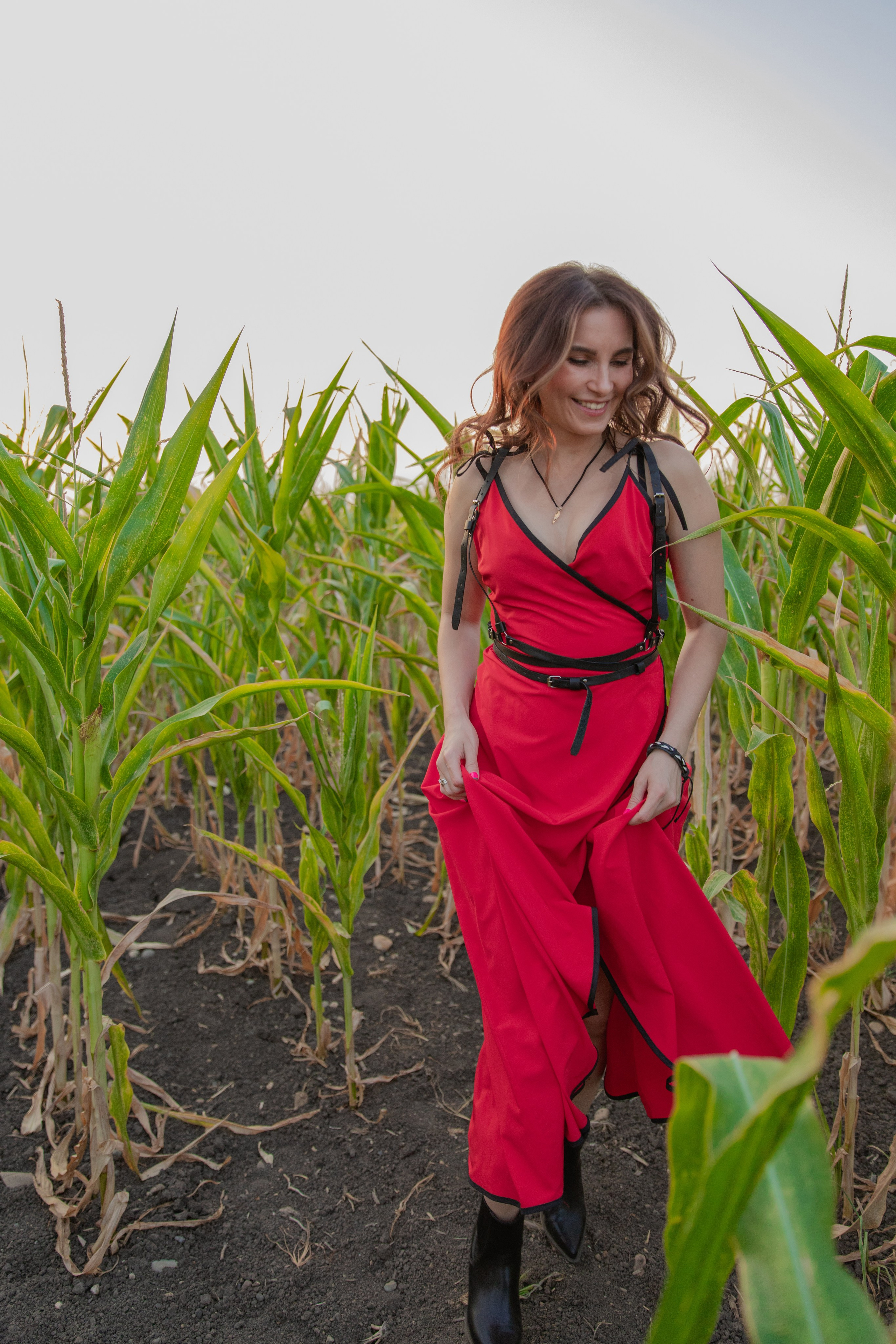 Красивая девушка  в красном платье бежит среди  высоких стеблей кукурузы на солнечном фоне