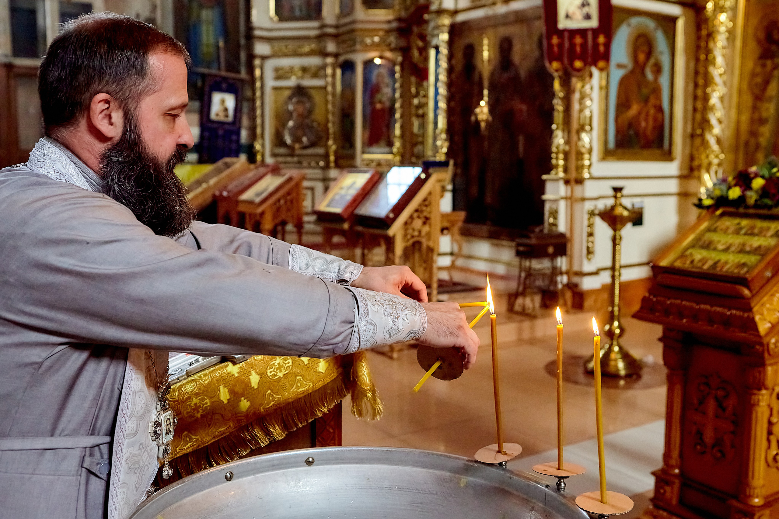 Священник у купели зажигает свечи
