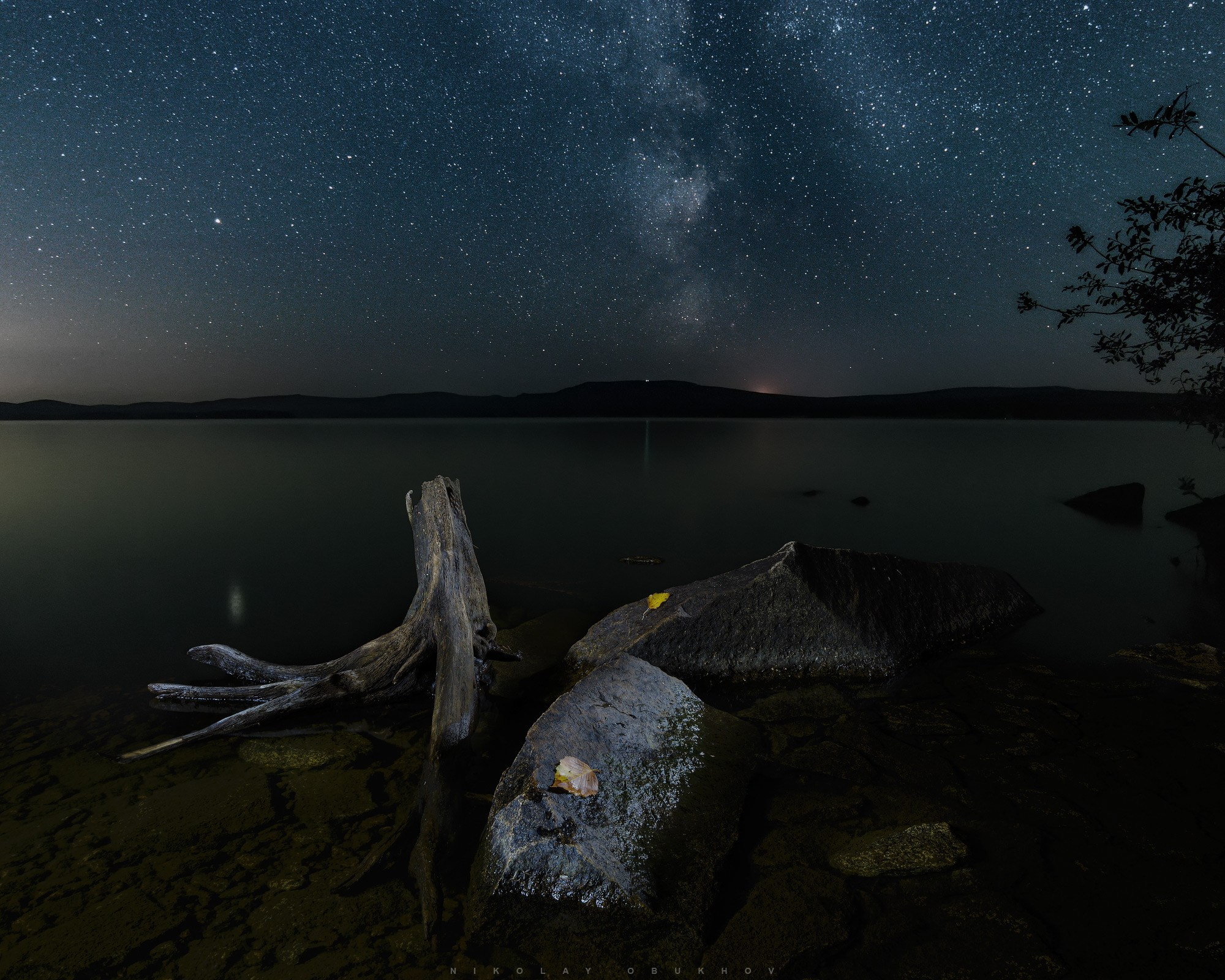 Красивый ночной пейзаж вдали от городов: звёзды отражаются в воде Черноисточинского пруда, Средний Урал.