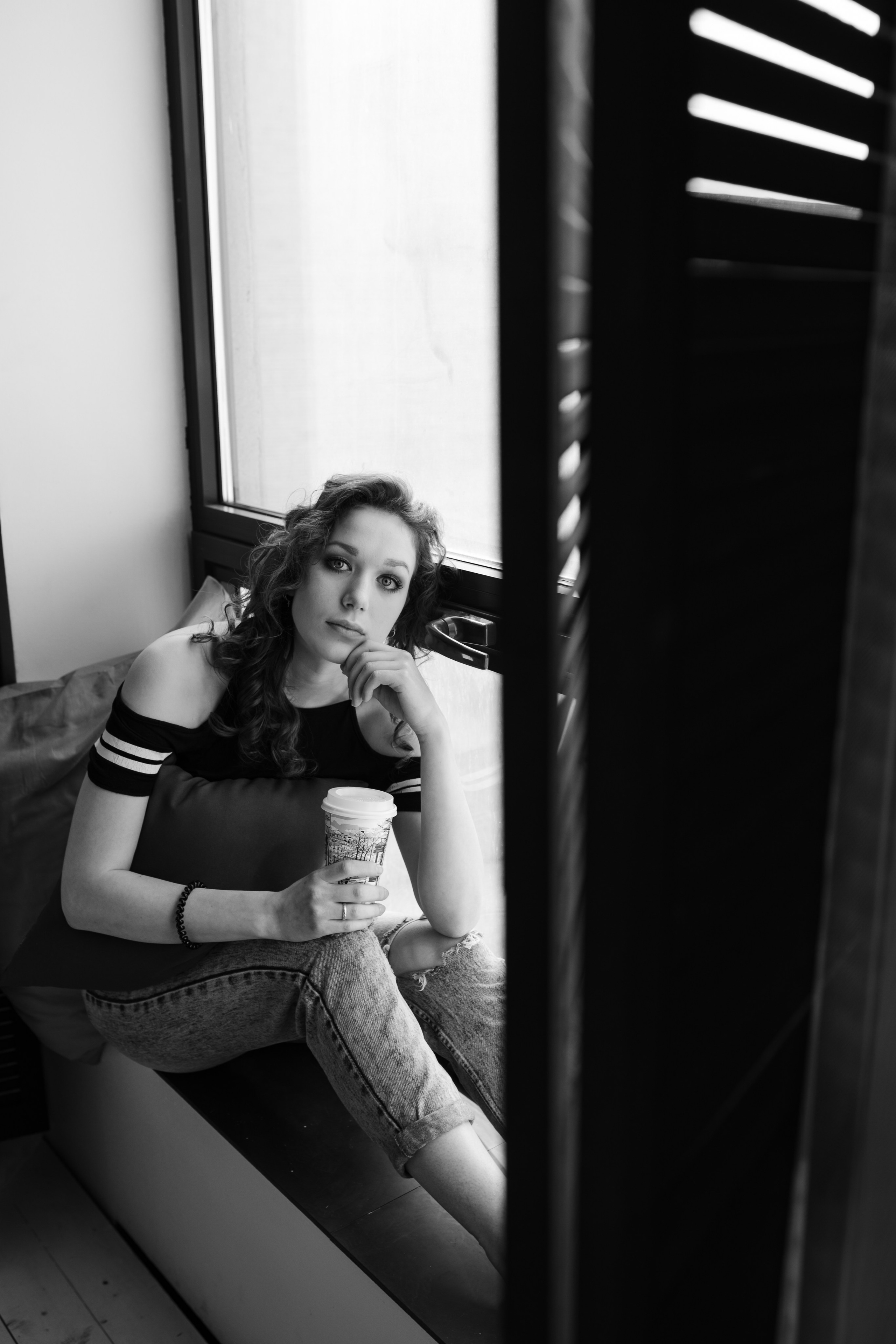 Девушка сидит на огромном окне пьет кофе И думает о приятном