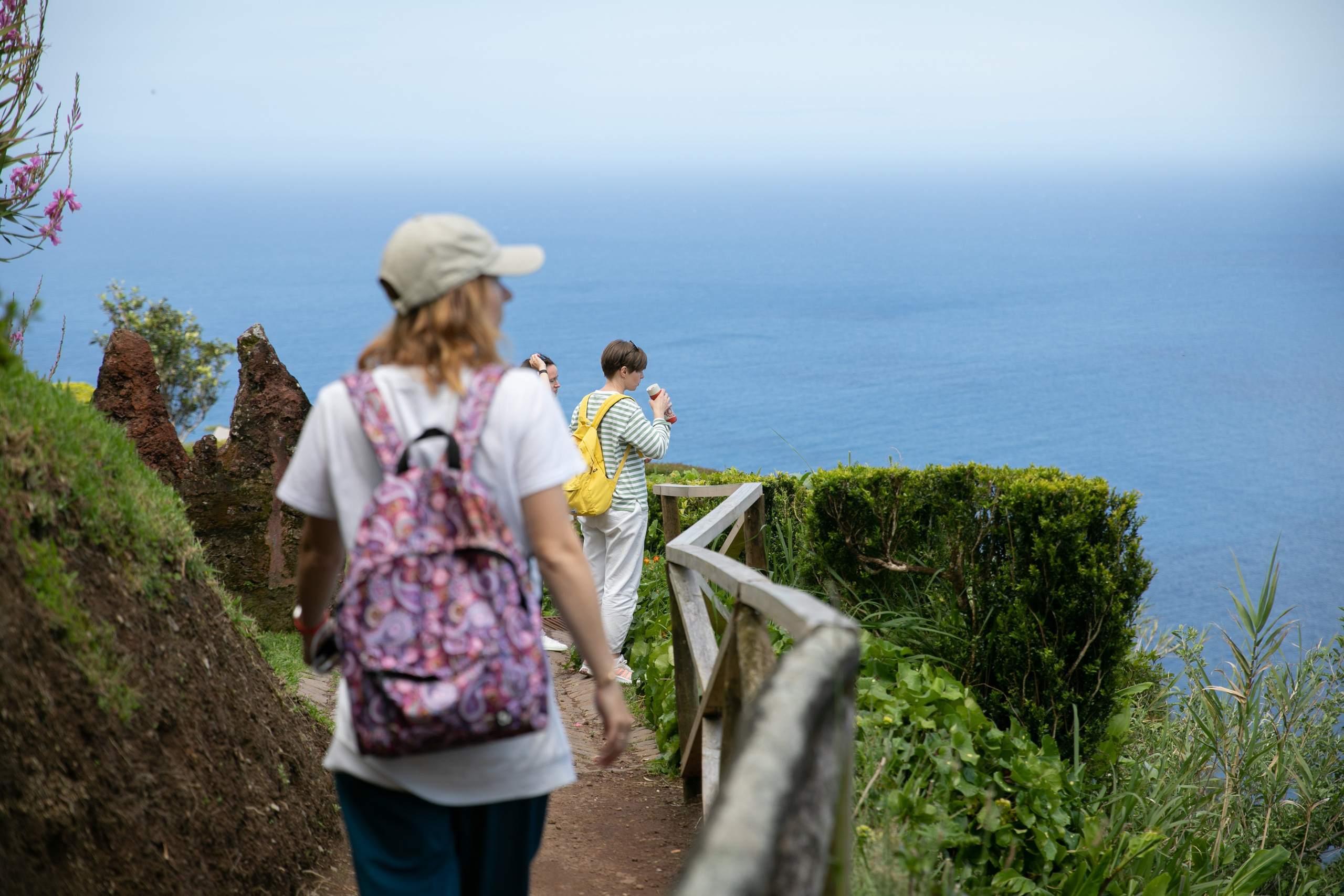 A group of young women walking through lush green landscapes, with the vast ocean and clear blue sky surrounding them on the Azores