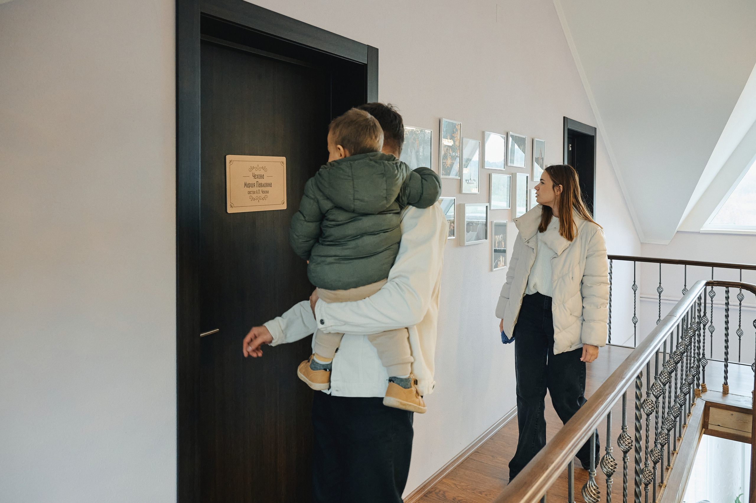 Отец с ребёнком на руках и мать в коридоре загородного отеля, у двери с табличкой.