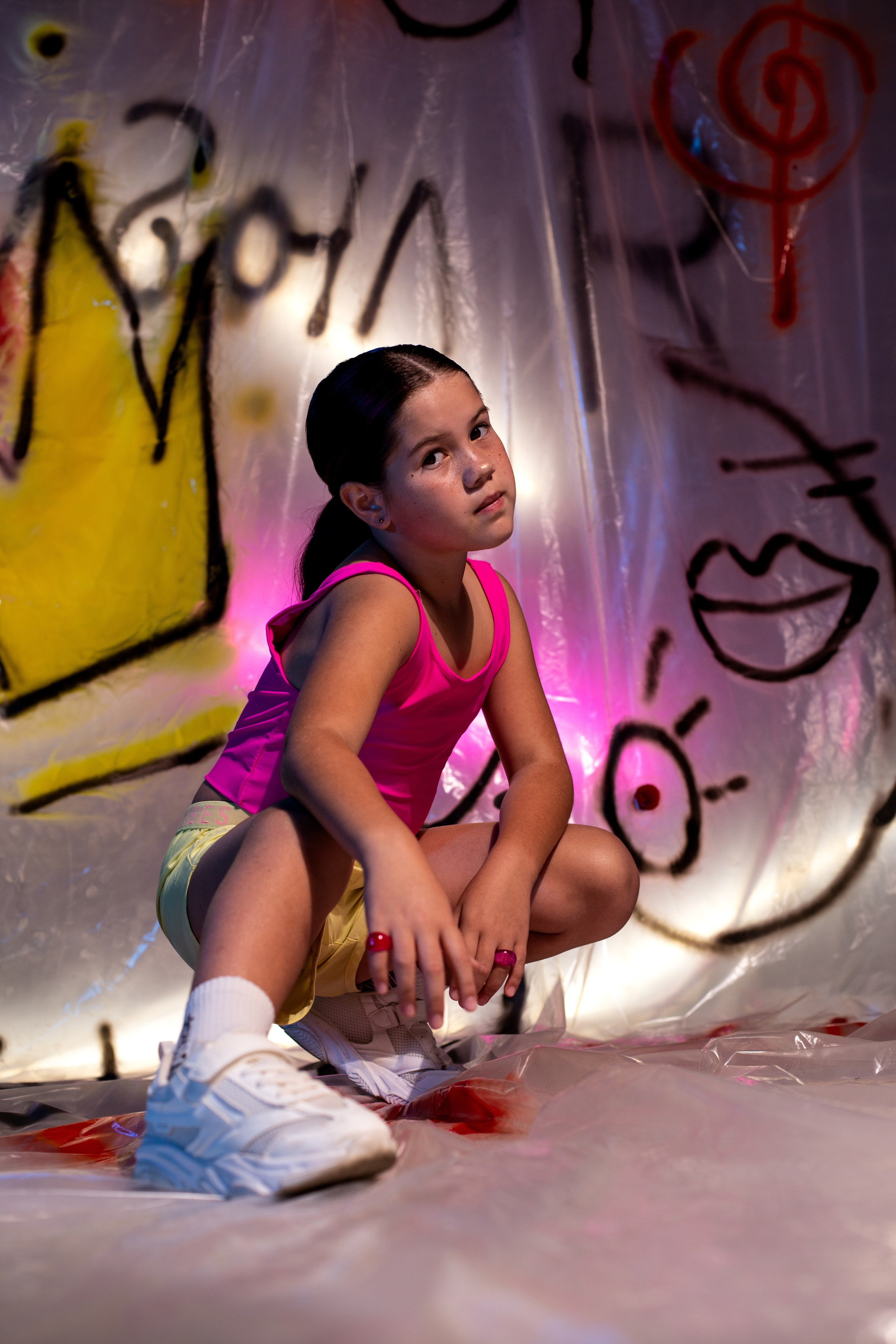 девочка позирует сидя в белых кроссовках и розовом топе