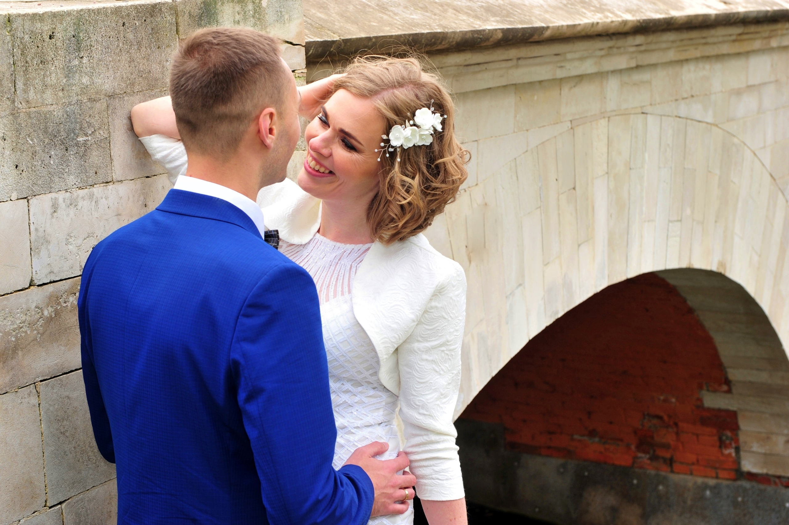 Свадьба в Царицыно хмурым прохладным летним днём, молодожены стоят у белого каменного моста в парке на фоне арки моста и воды