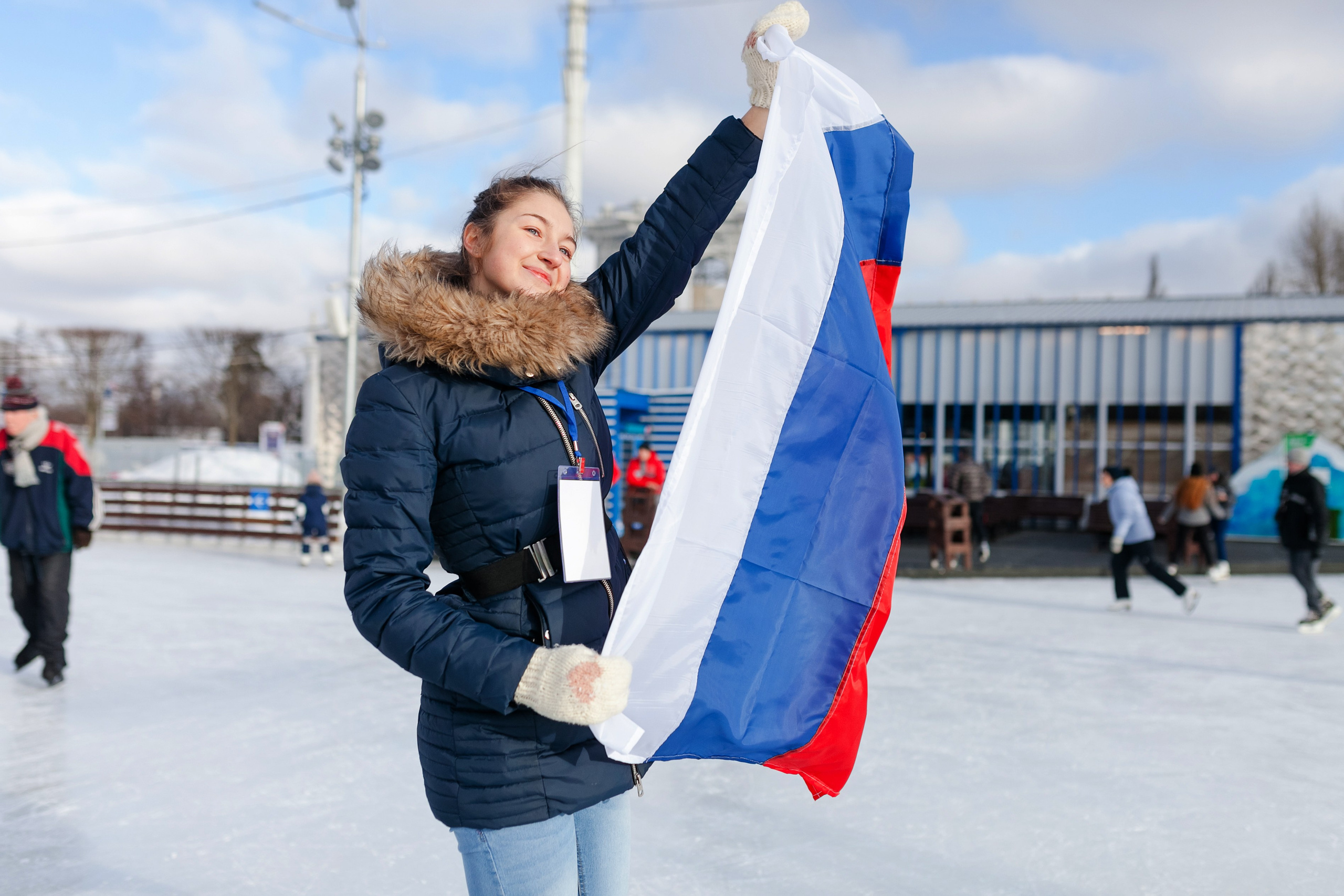 Девушка на катке ВДНХ держит в руках развевающийся российский флаг