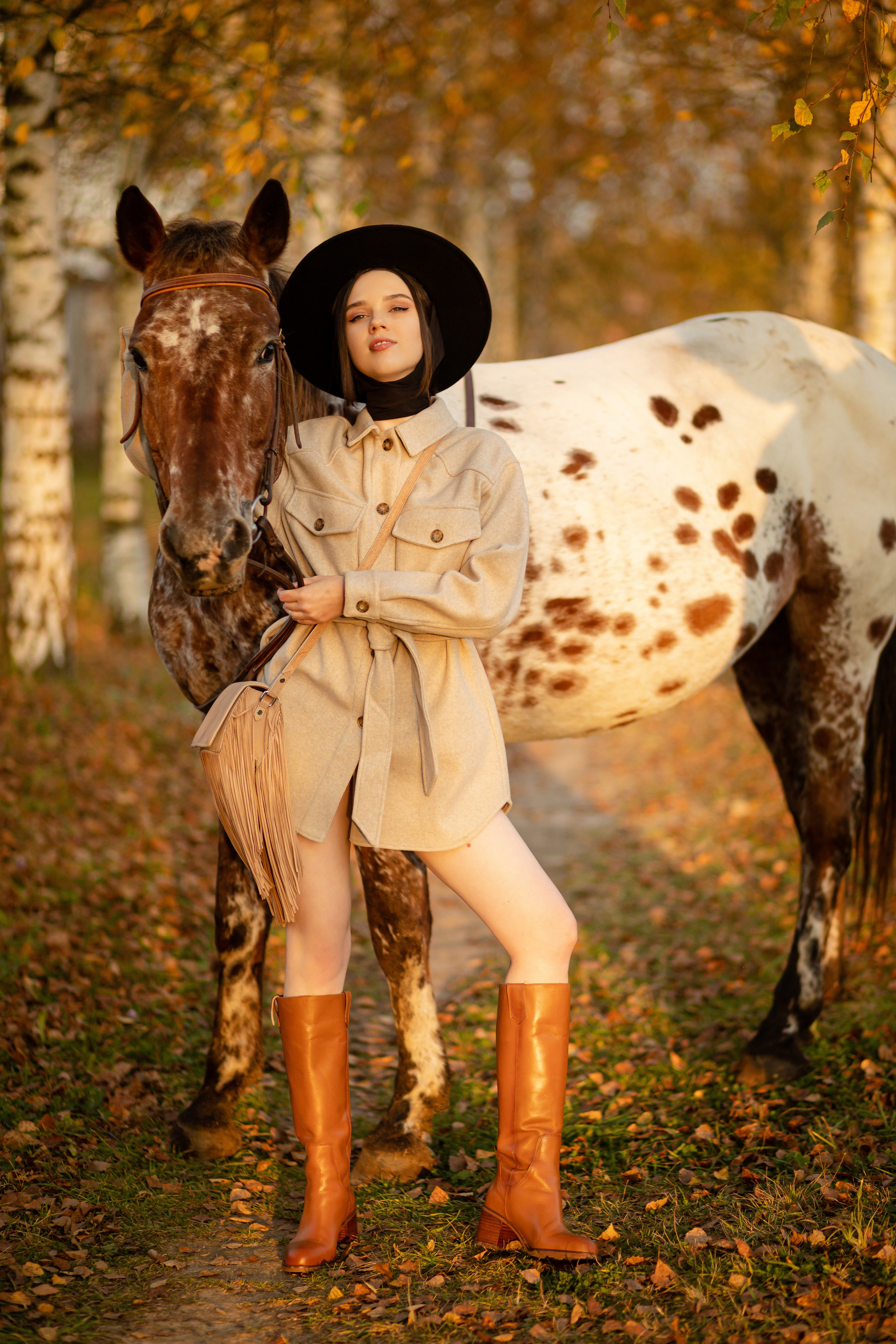 Девушка обутая в красные сапоги стоит с лошадью на фоне берез.