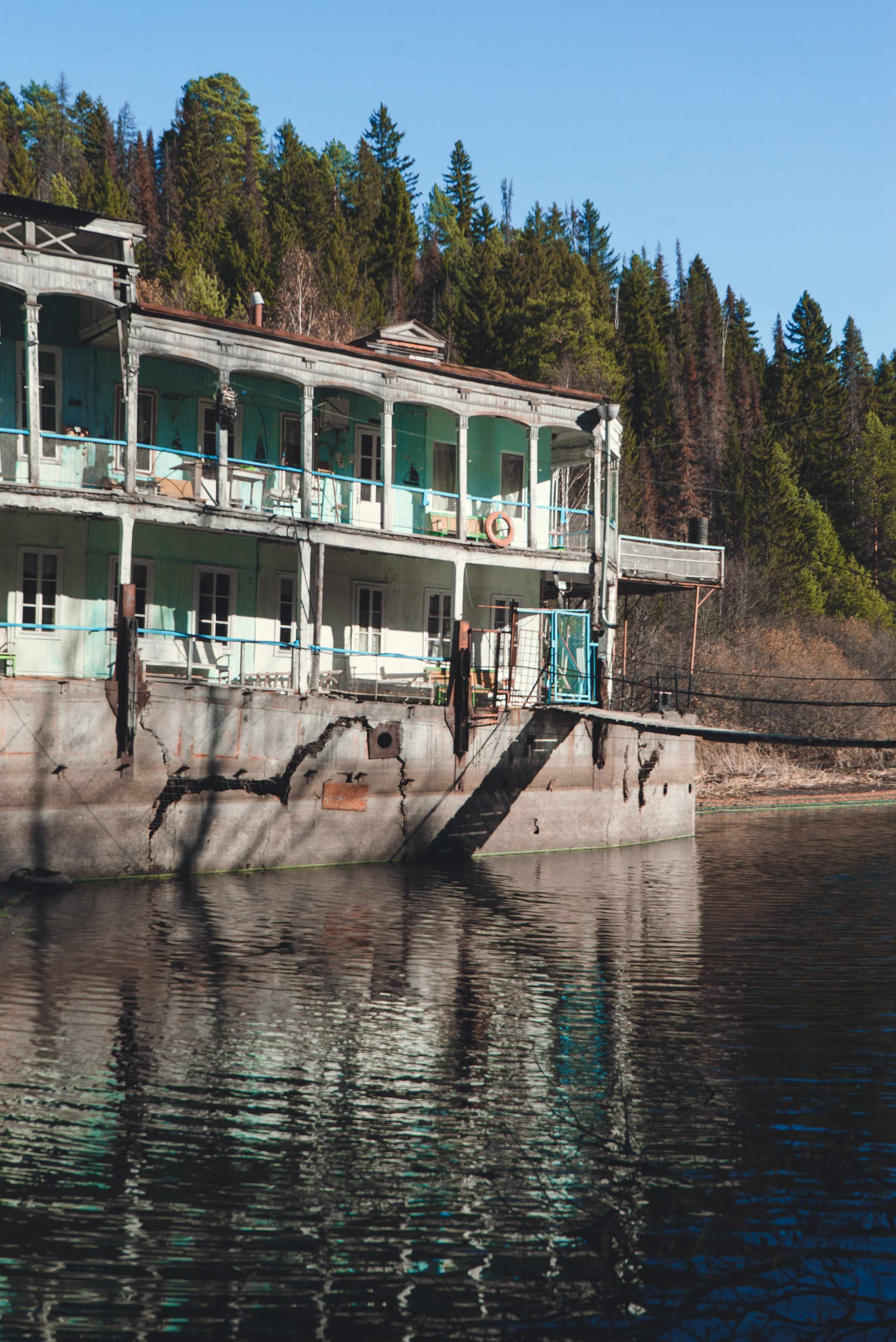 Заброшенное здание, виднеющееся на старинном берегу речной пароход, стоит на водоеме среди густого леса. Его фасад украшен колоннами и балконами, однако здание выглядит ветхим и запущенным: краска облупилась, металл покрыт ржавчиной. Вокруг голые деревья и хвойные леса, что создает ощущение уединенности и застенчивости.