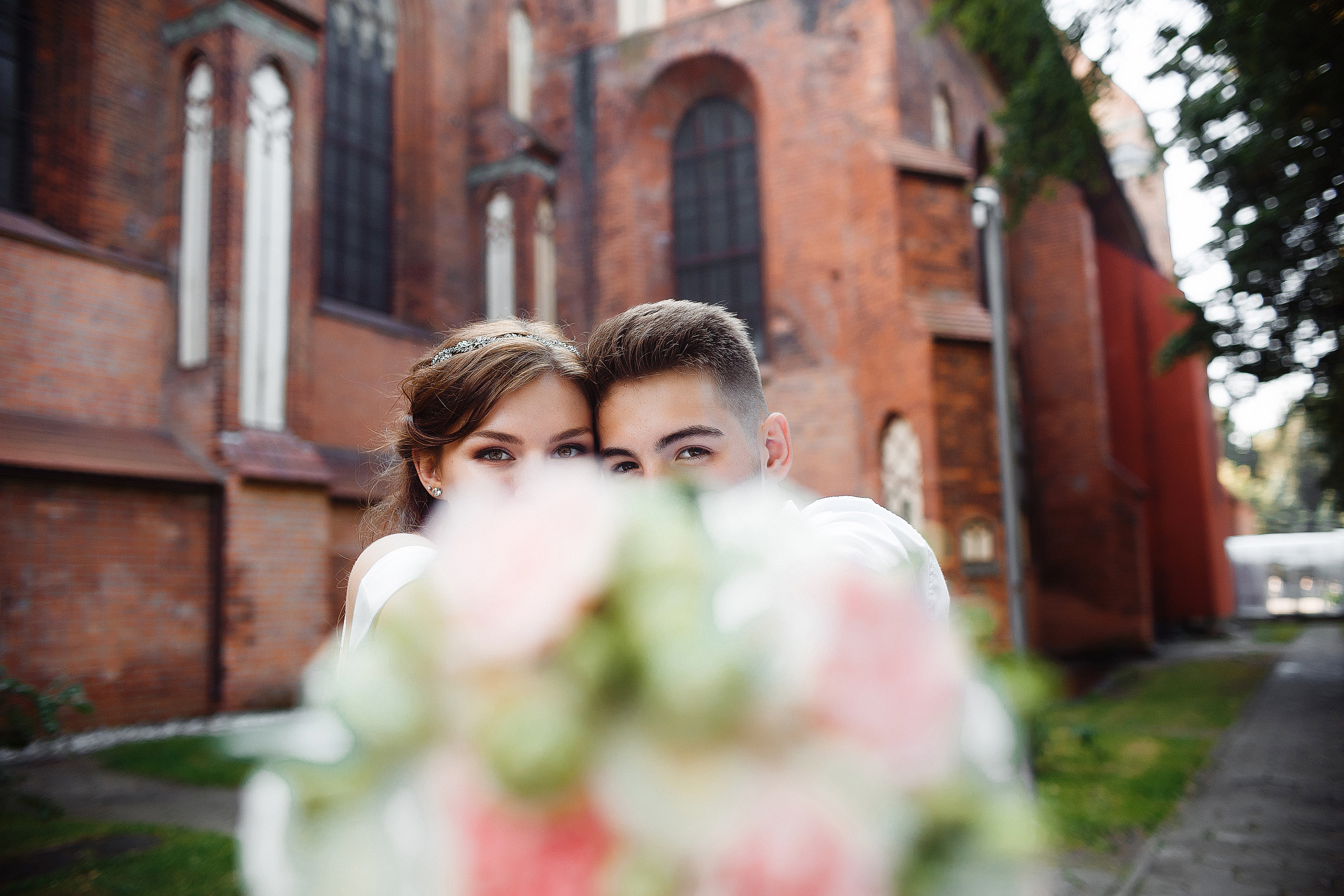 Жених и невеста выглядывают из-за свадебного букета