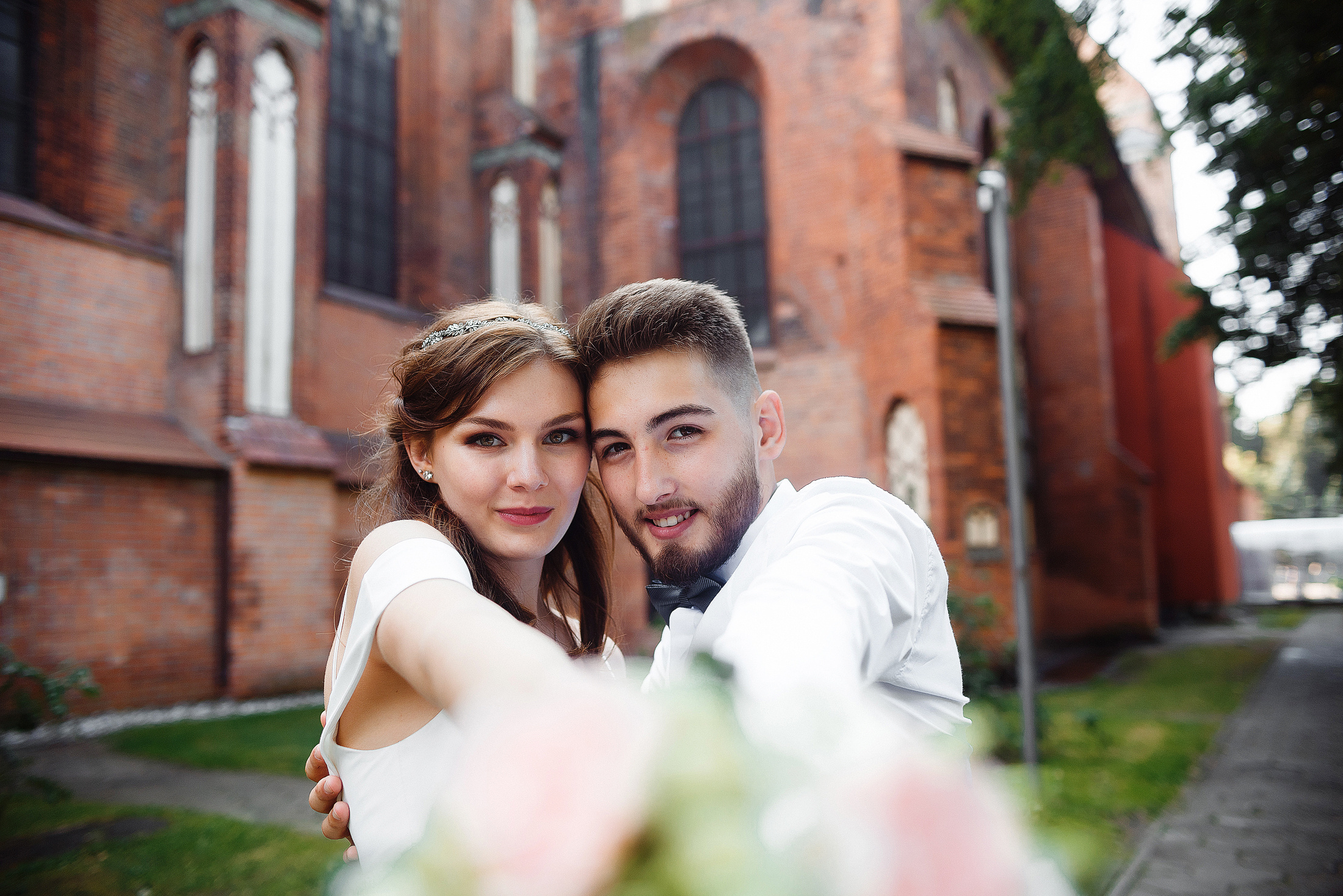 Жених и невеста позируют на фоне Кафедрального собора и держат на вытянутых руках свадебный букет