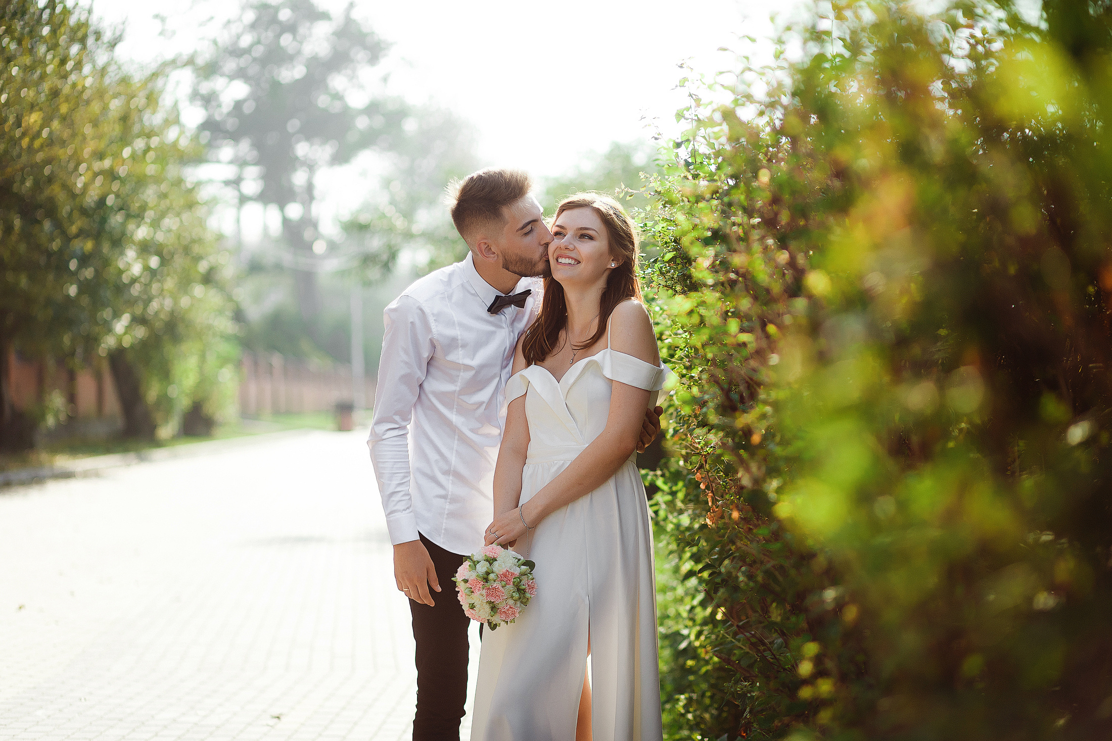 Жених целует невесту в белом платье в парке на закате