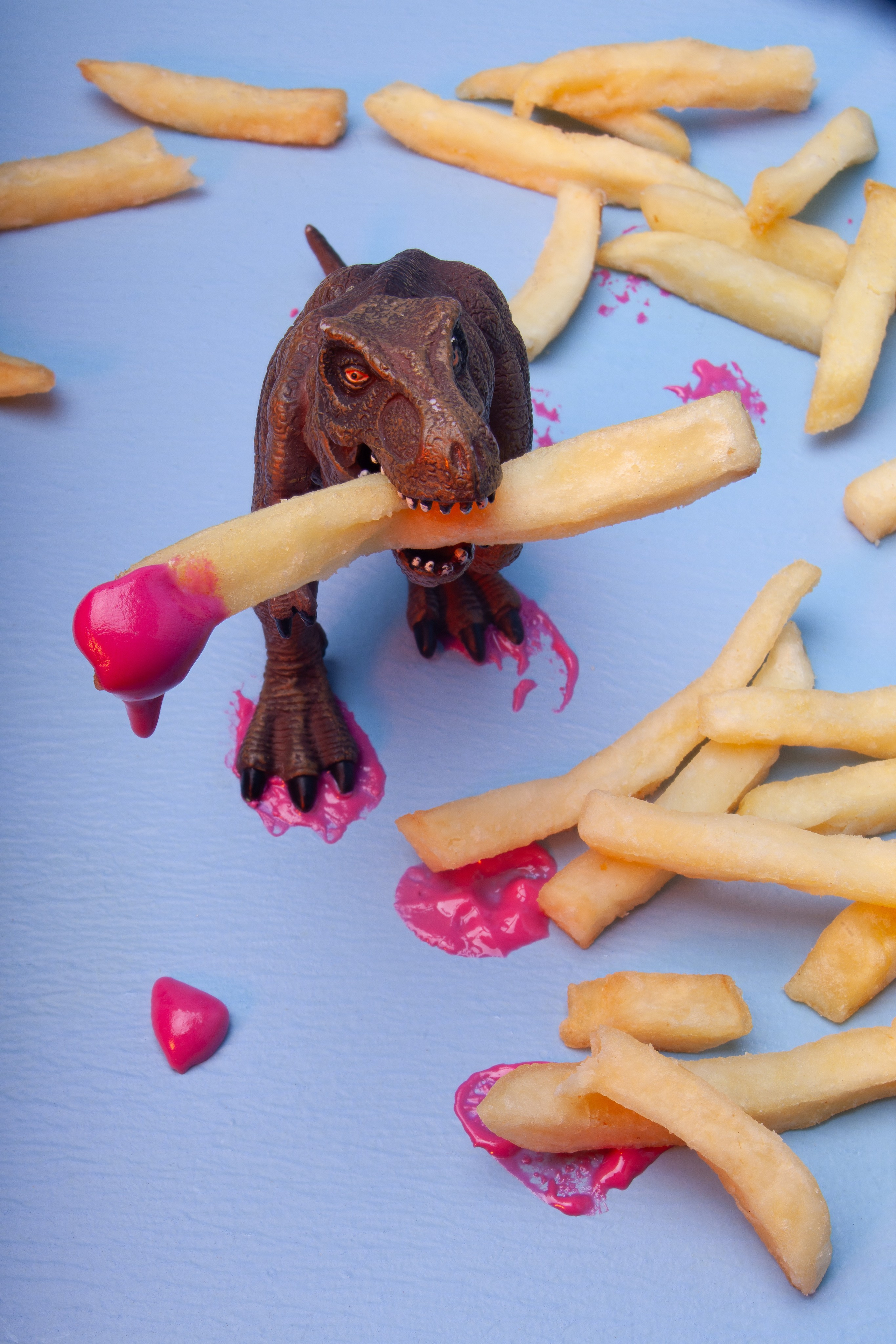 тиранозавр держит в зубах картофель фри с фиолетовыми каплями крема