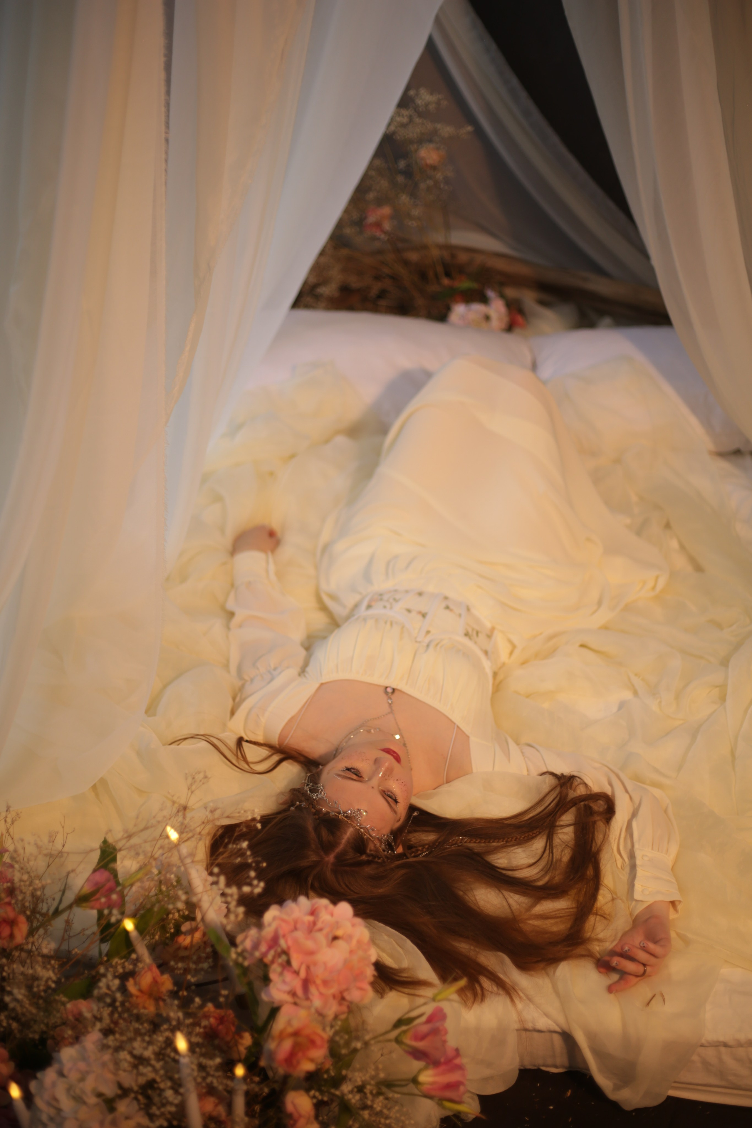 Фотография эльфийки в Перми: девушка в белом платье лежит на кровати под балдахином среди цветов и свечей