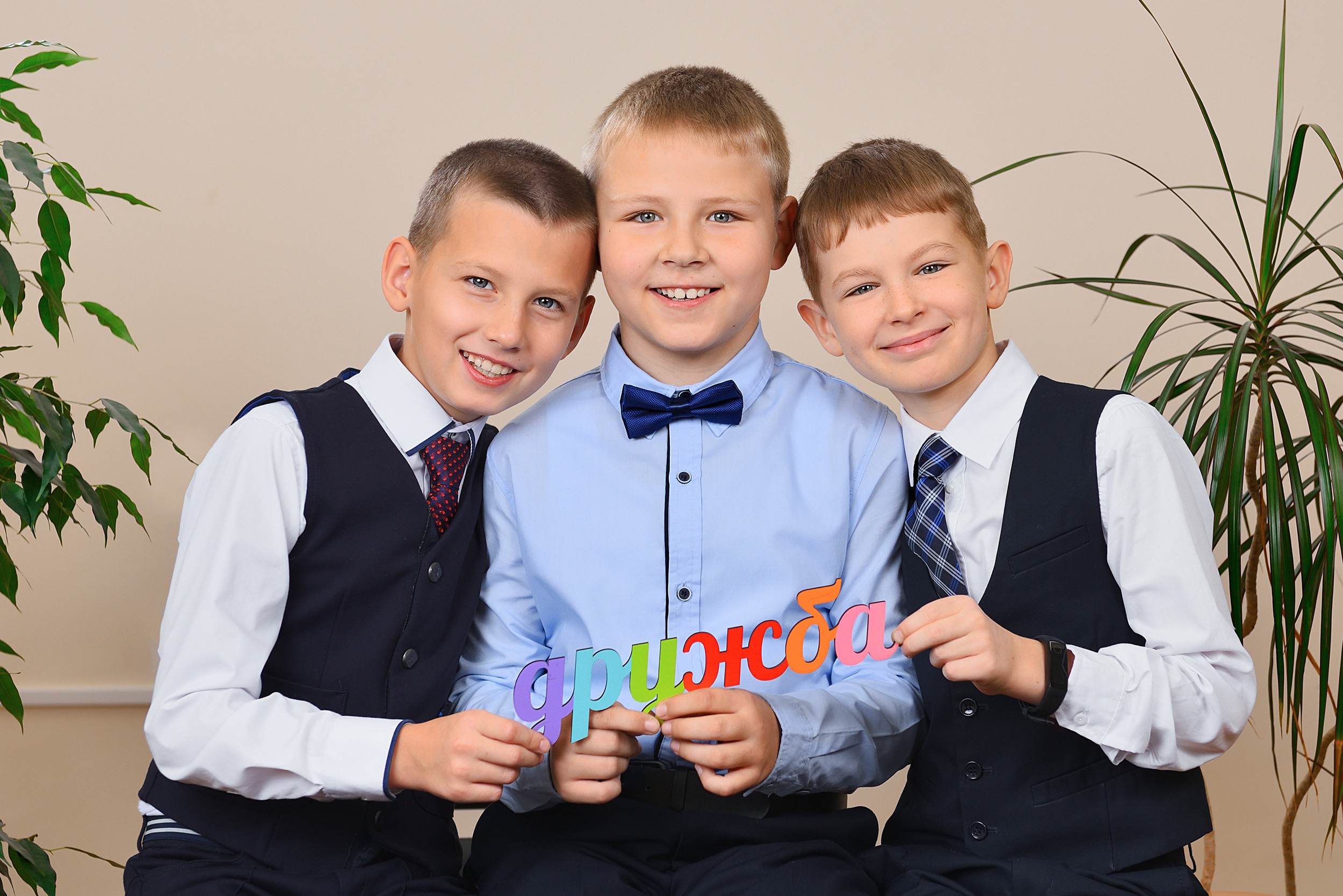 Школьники держат табличку со словом "дружба" и обнимают друг друга.