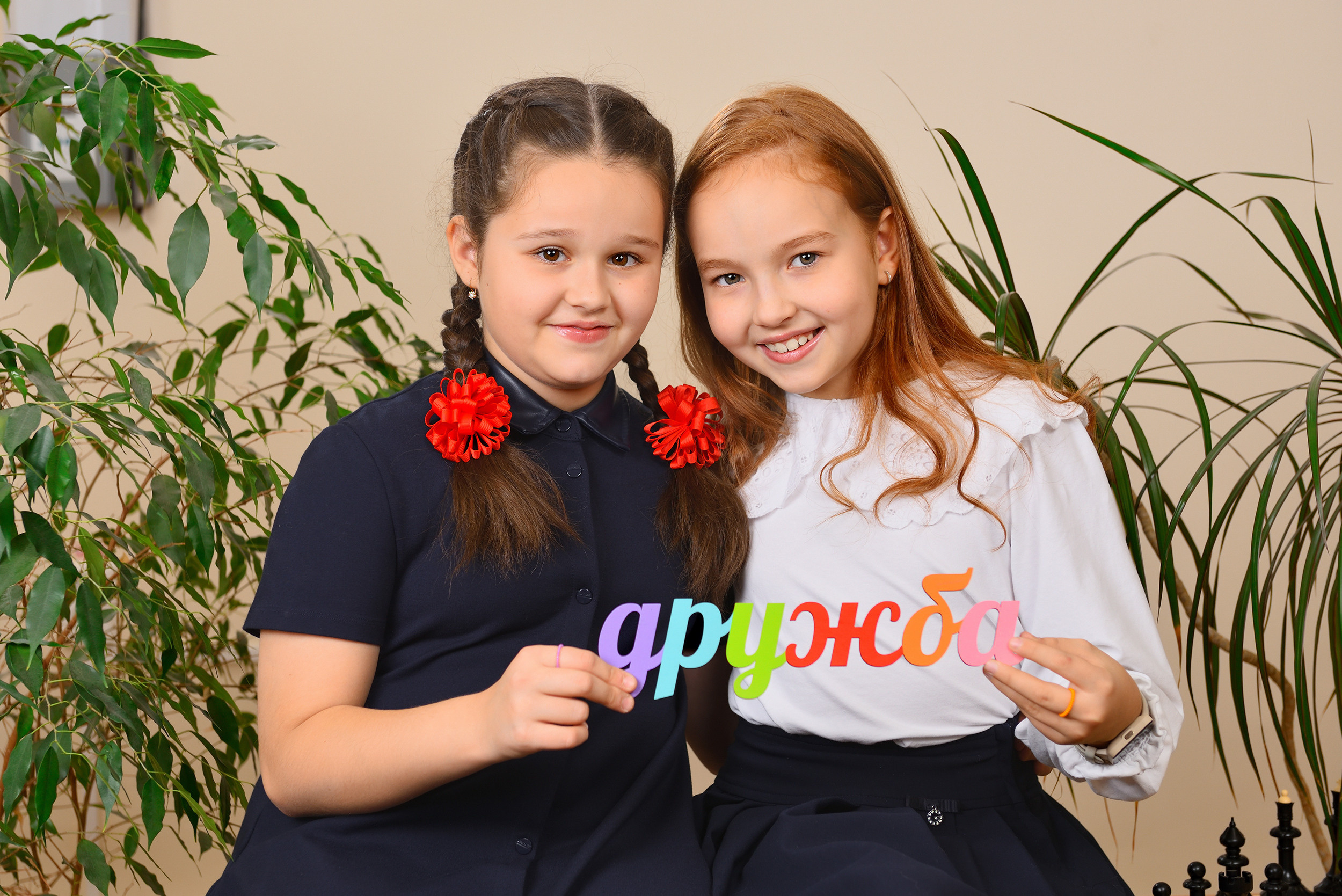 Две школьницы держат табличку со словом "дружба" и обнимают друг друга.