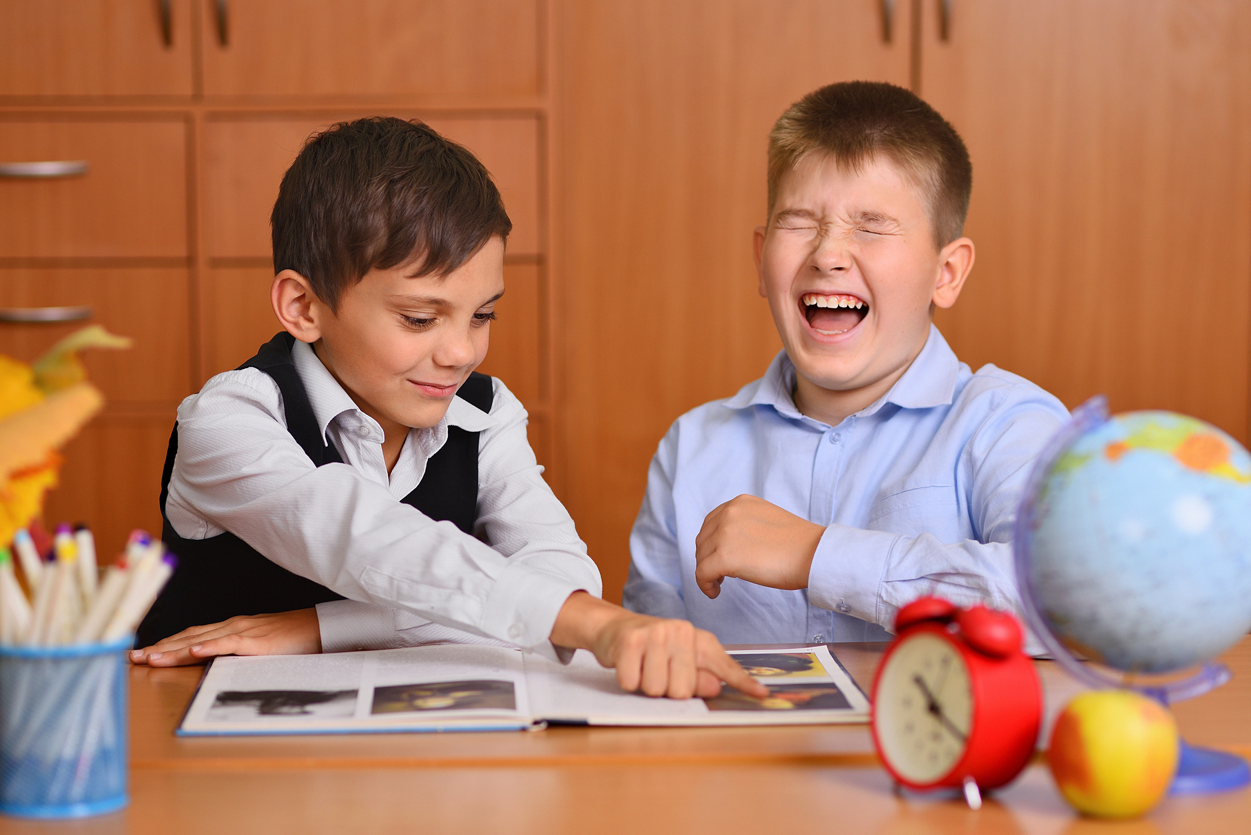 Смеющиеся школьники весело рассматривают книгу, сидя за партой в классе.