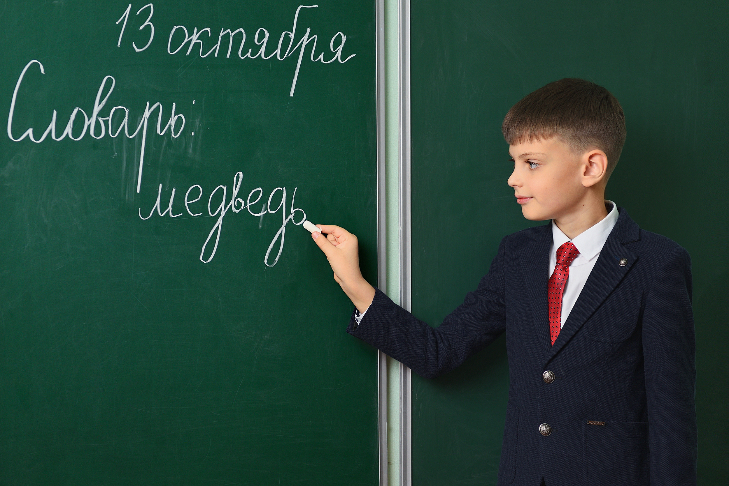 Школьник держит мел и пишет что-то на школьной доске.