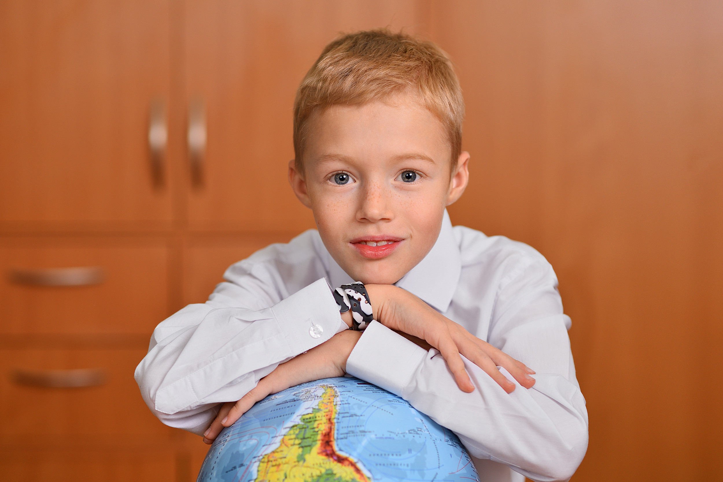 Крупный портрет школьника, лежащего на глобусе.