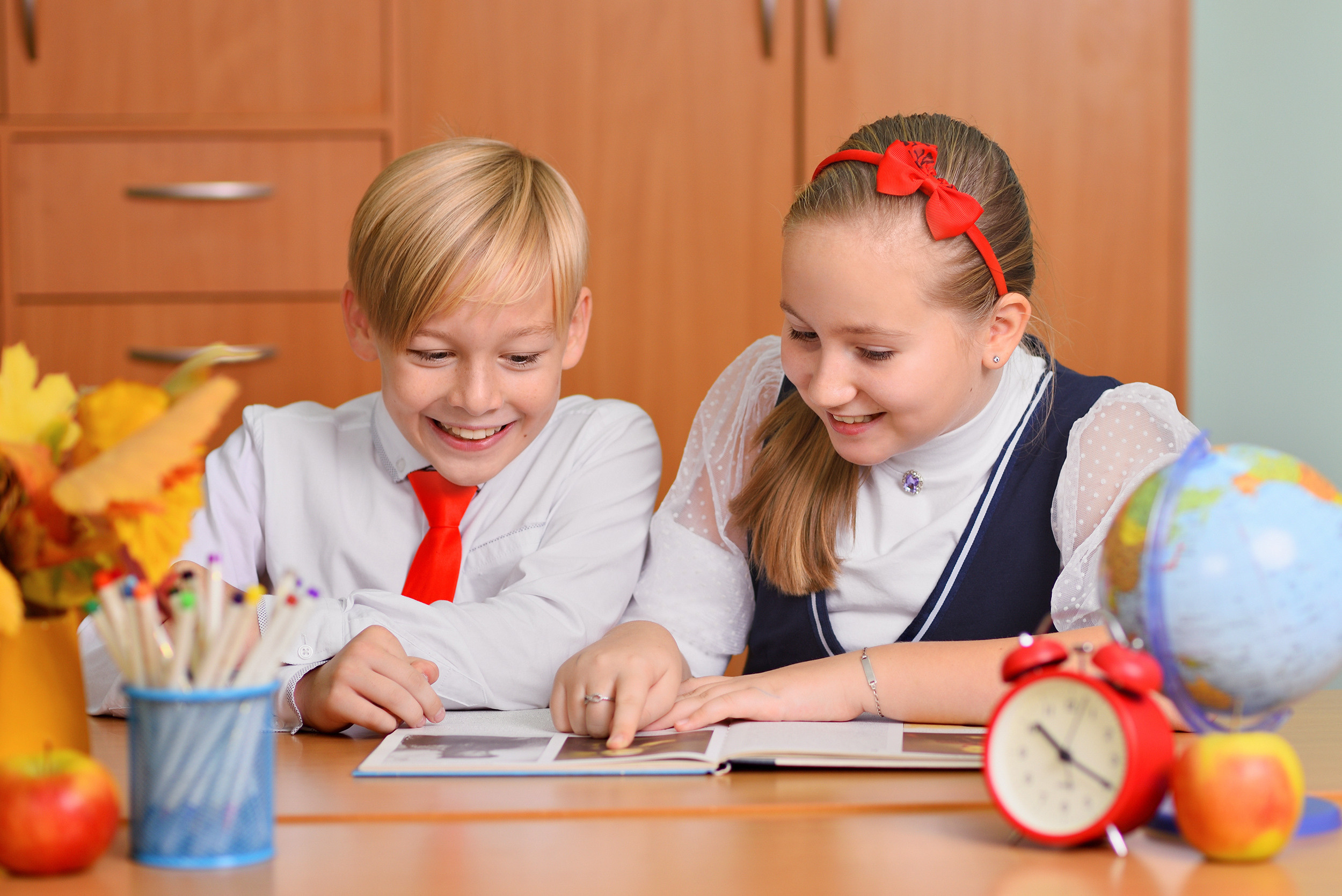Улыбающиеся школьник и школьница весело рассматривают книгу, сидя за школьной партой.